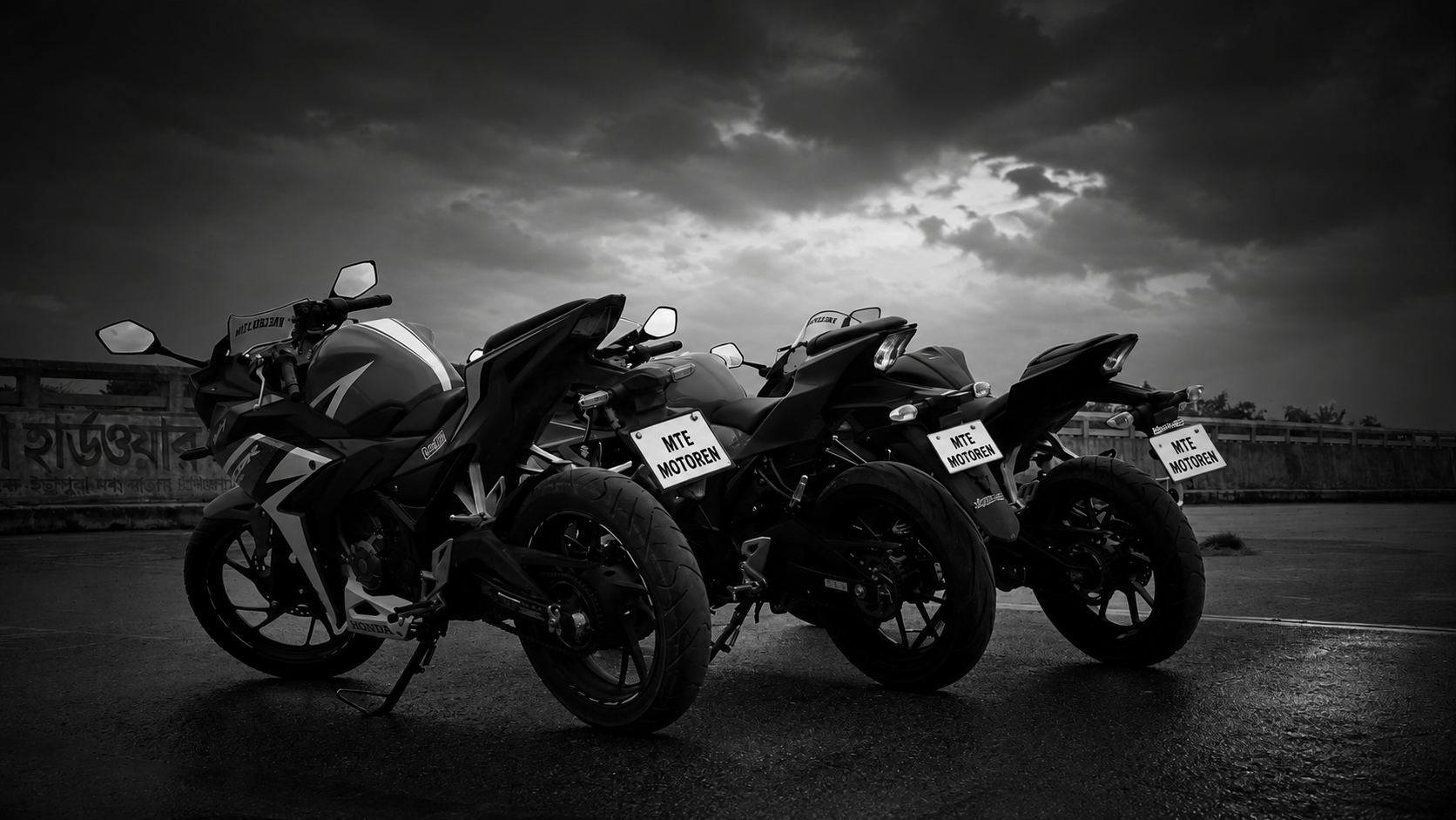 Drie donkere sportmotoren geparkeerd op een open asfaltoppervlak onder een bewolkte hemel, elk met kentekenplaten die luiden "MTE MOTORREN."