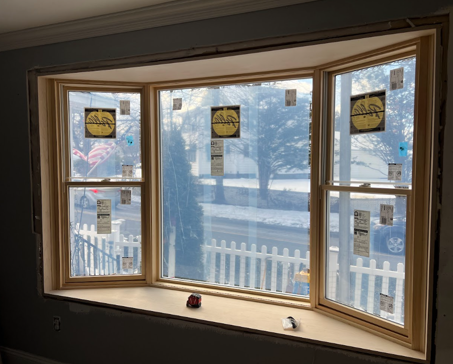 Newly installed double-pane window with protective stickers on glass, installed in a wall frame with a construction area visible outside.