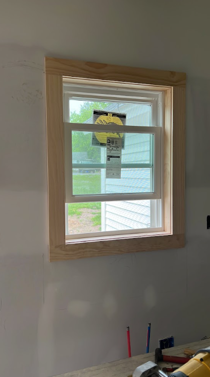 Newly installed window with a wooden frame in a room under construction, with tools and supplies on a workbench below.