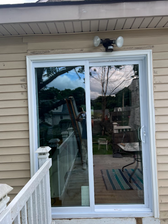 Backyard view through a glass sliding door, with outdoor furniture and a striped rug visible inside and outside, and a light fixture above the door.