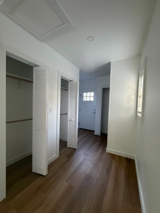 Empty room with white walls, hardwood floors, closet with louvered doors, and a white front door with a small window.