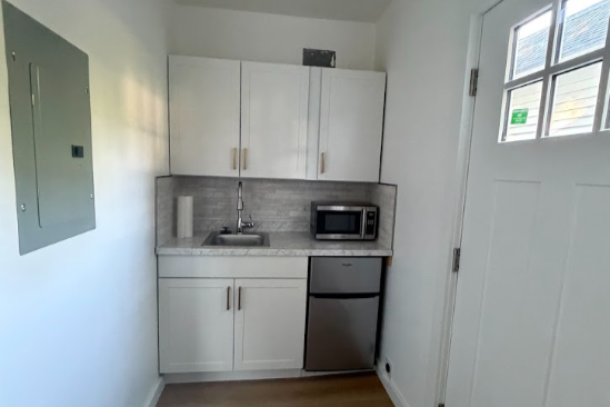 Small kitchenette with white cabinets, a microwave, mini refrigerator, sink, and a paper towel roll.
