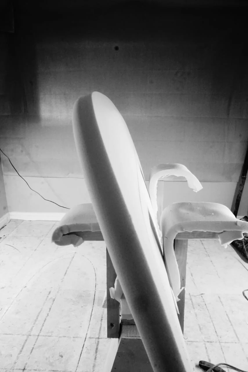Black and white photo of a surfboard on a stand in a room with a wooden ceiling and tiled floor.
