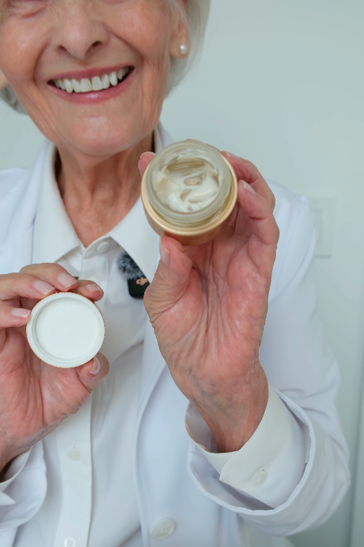 Happy elderly woman holding an open jar of cream or moisturizer, demonstrating its smooth texture.