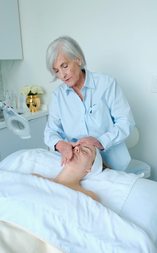 A woman receiving a facial treatment from an aesthetician in a spa or clinic setting.