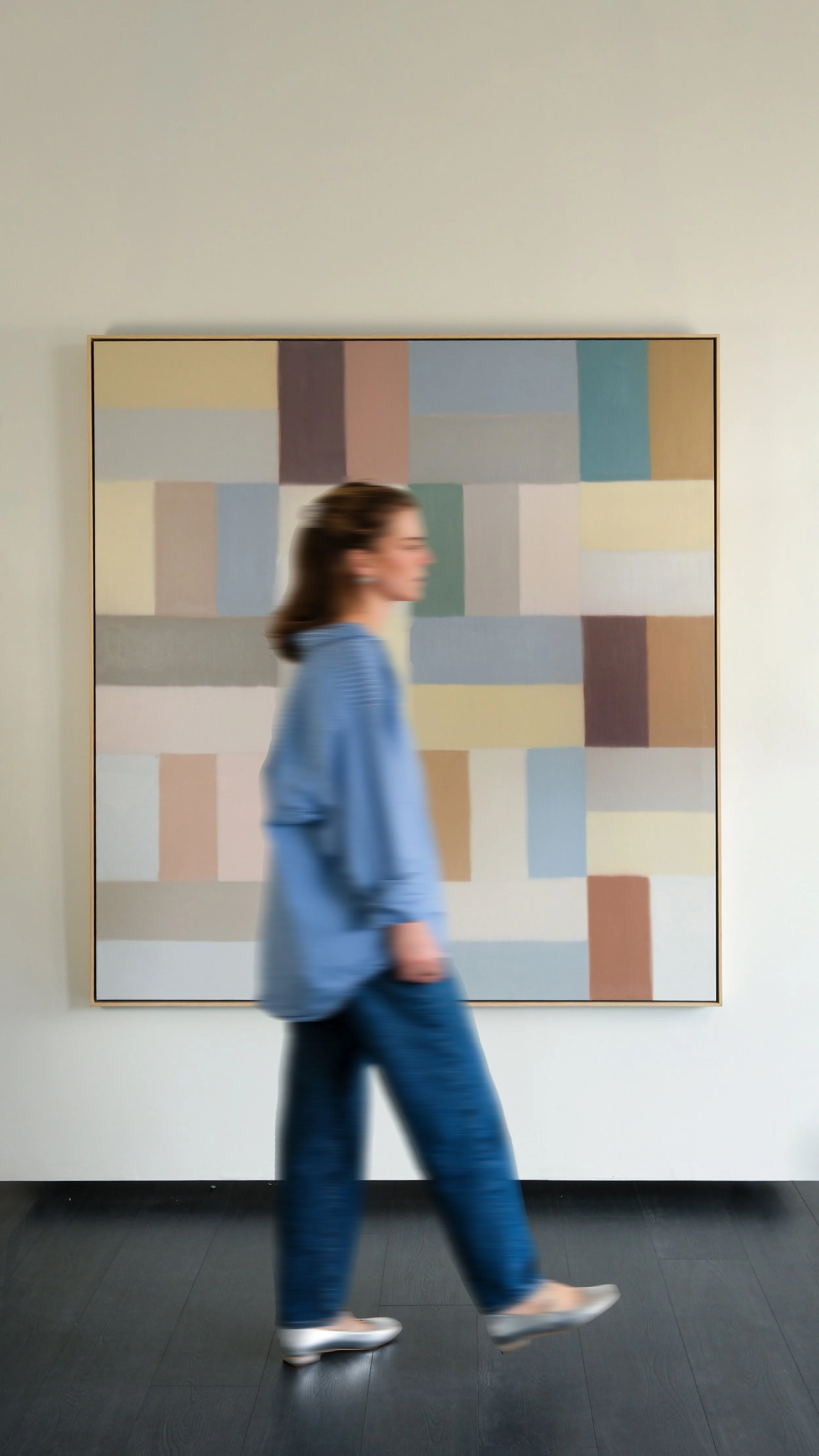 A woman walking past a large abstract painting with blocks of pastel colors on a white gallery wall.
