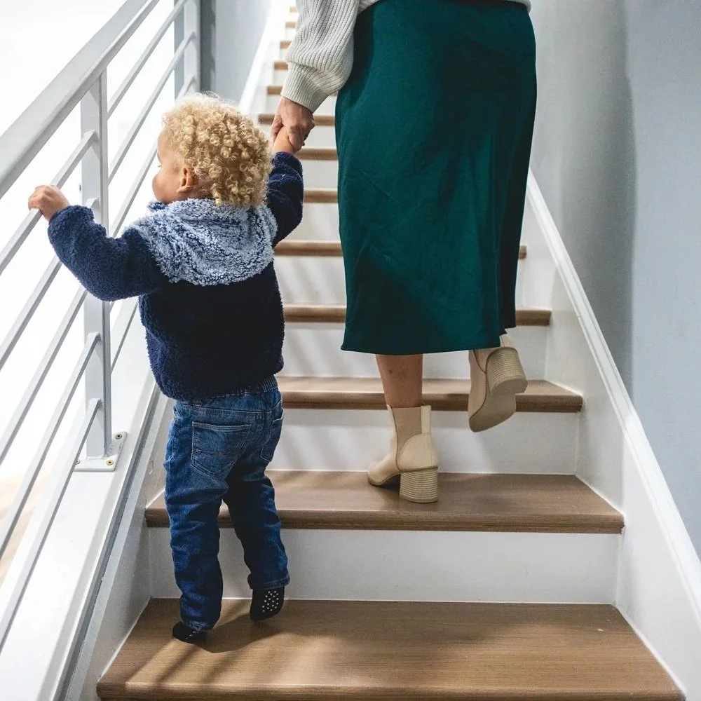 A child holding an adult's hand while walking up stairs, with both facing away from the camera.