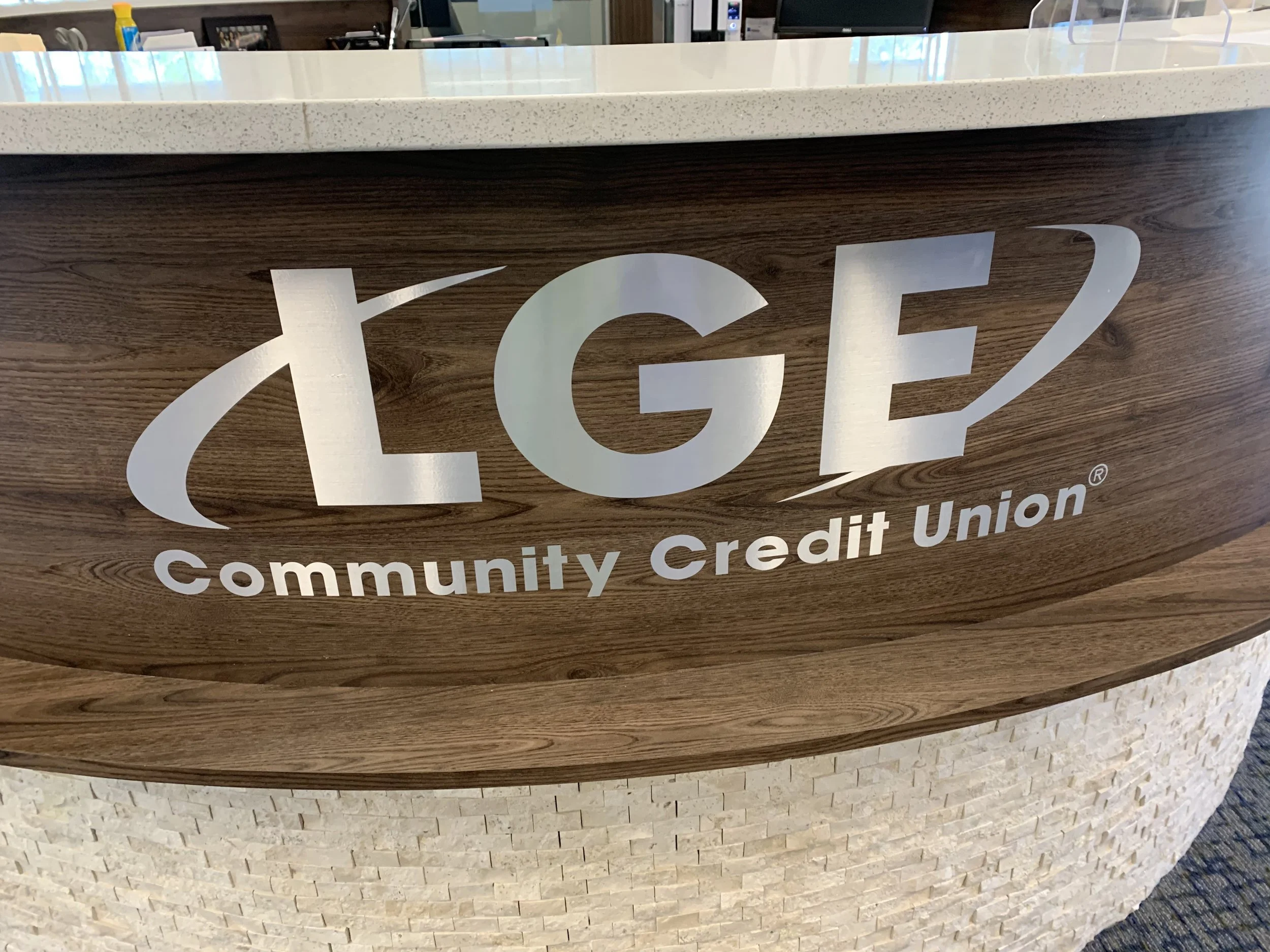 Close-up of a reception desk with the logo and name of a community credit union, featuring a wood finish and a white speckled countertop.