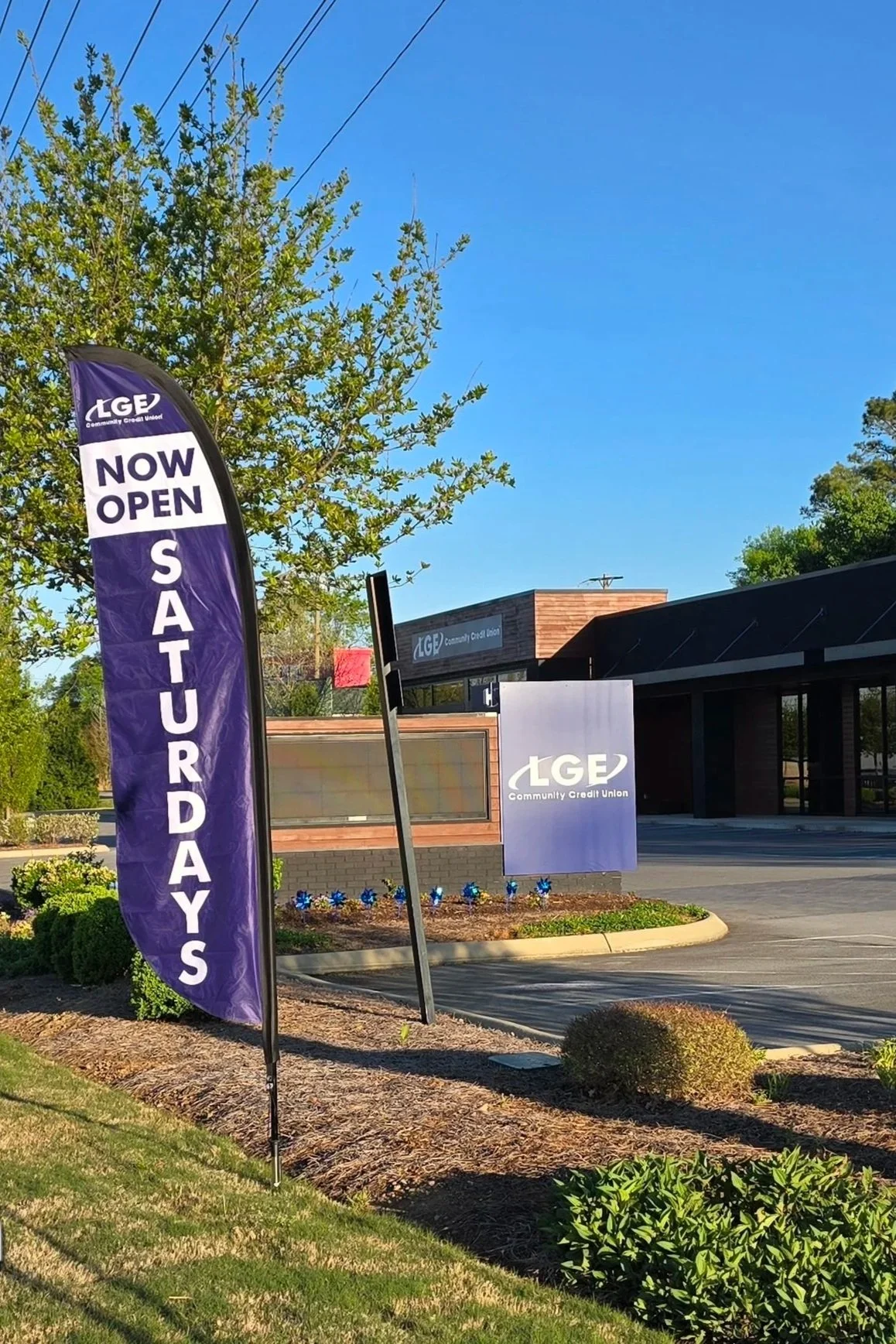 Flag and sign outside a community credit union with the text 'Now Open Saturdays' indicating the bank's operating hours.