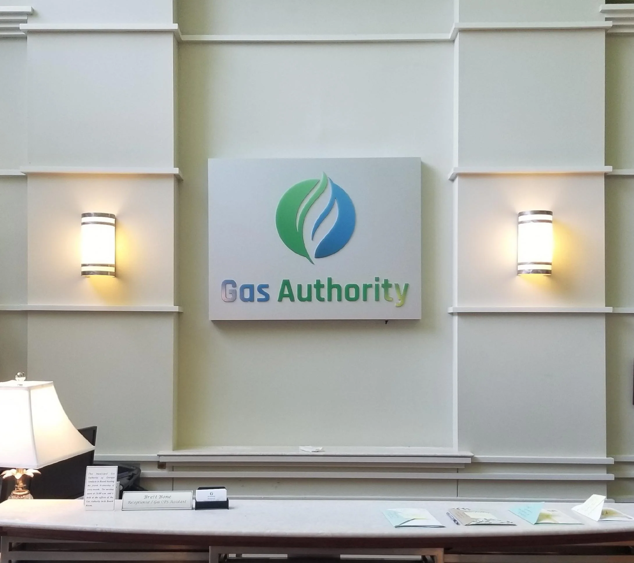 A display with the Gas Authority logo in a room with cream-colored walls and two wall-mounted lights. There are signs on a table below the display, including one that reads 'Brett Bone.'