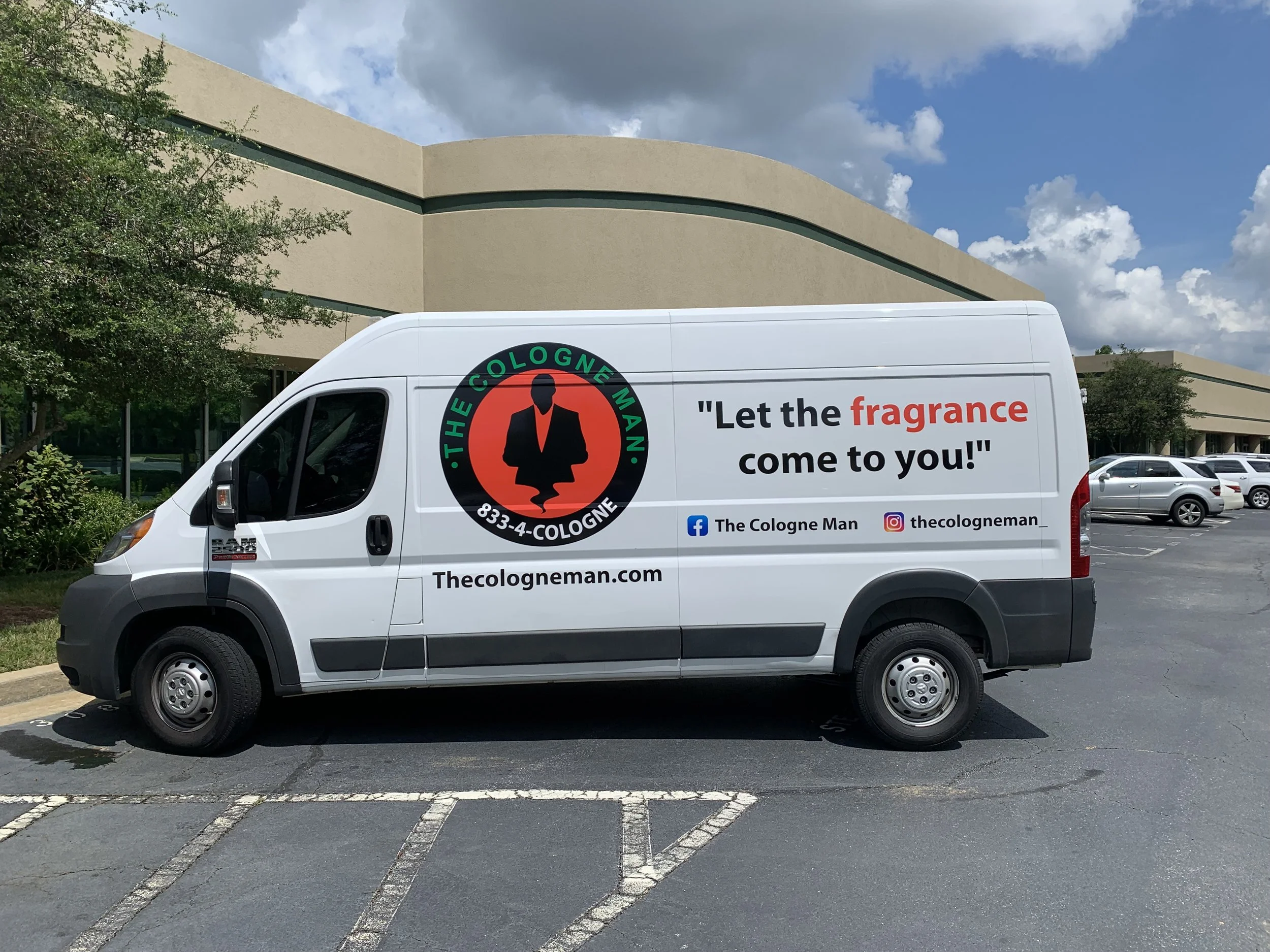 White van parked in a parking lot with a large advertisement on the side, featuring a logo of a person in a suit and the text 'Let the fragrance come to you!' along with social media icons and website information.