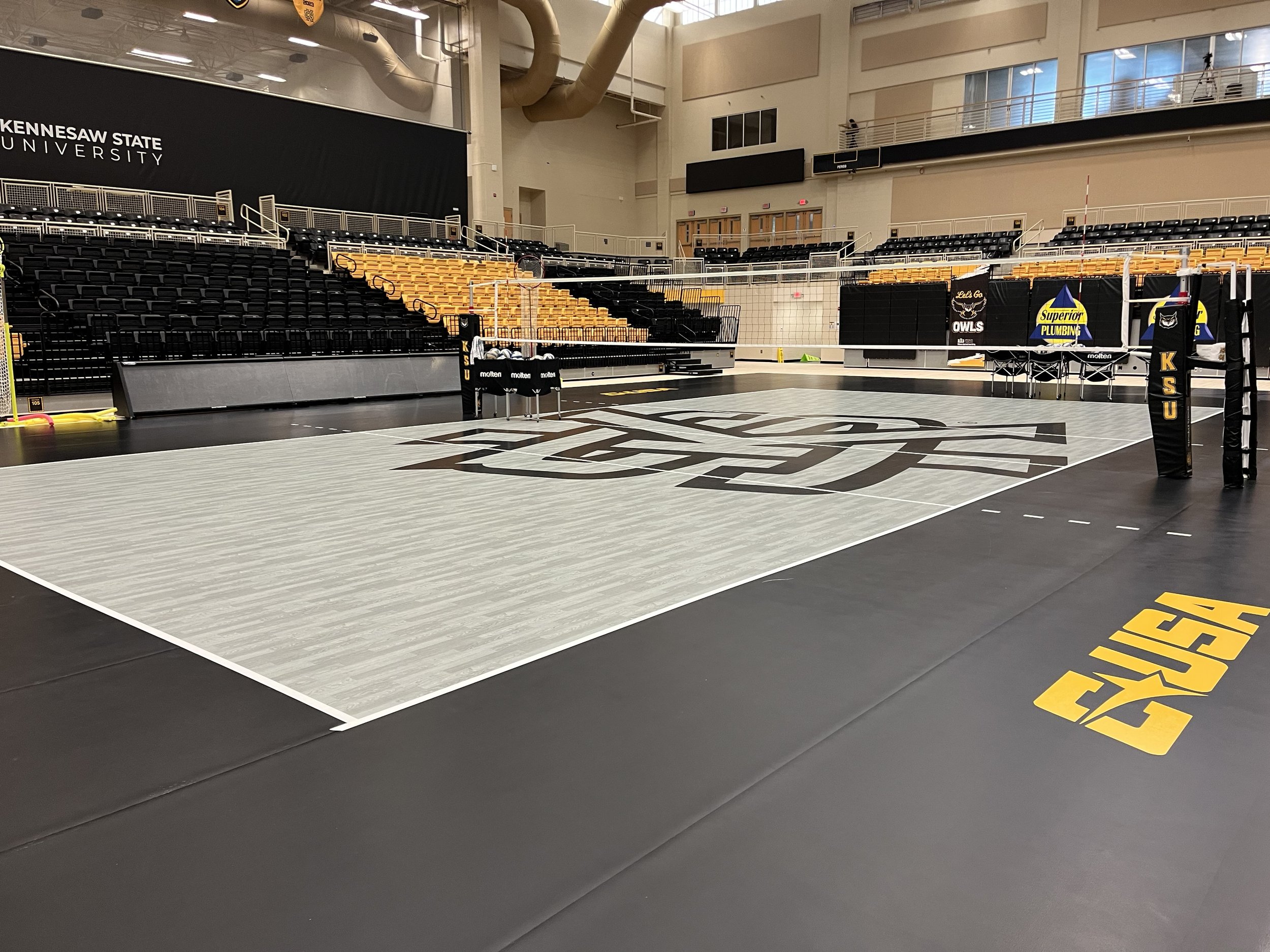 Indoor volleyball court with black and yellow seating, volleyball net, and sports banners inside a gymnasium at Kennesaw State University.
