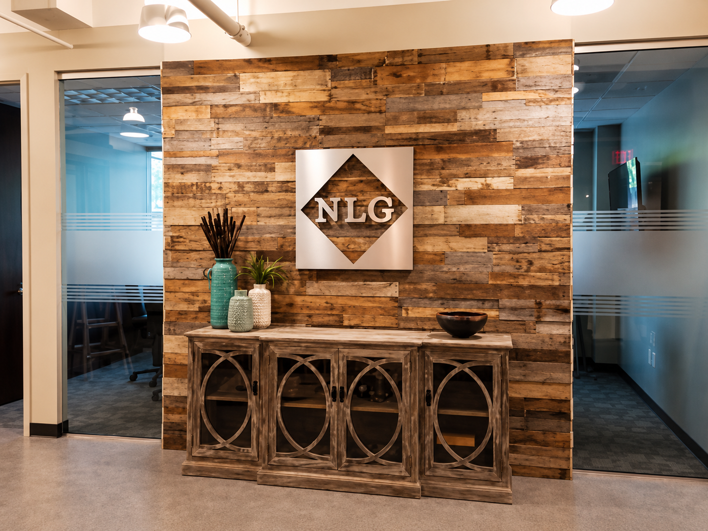 Interior office lobby with rustic wood wall, metal NLG sign, wooden cabinet with decorative vases and bowl.