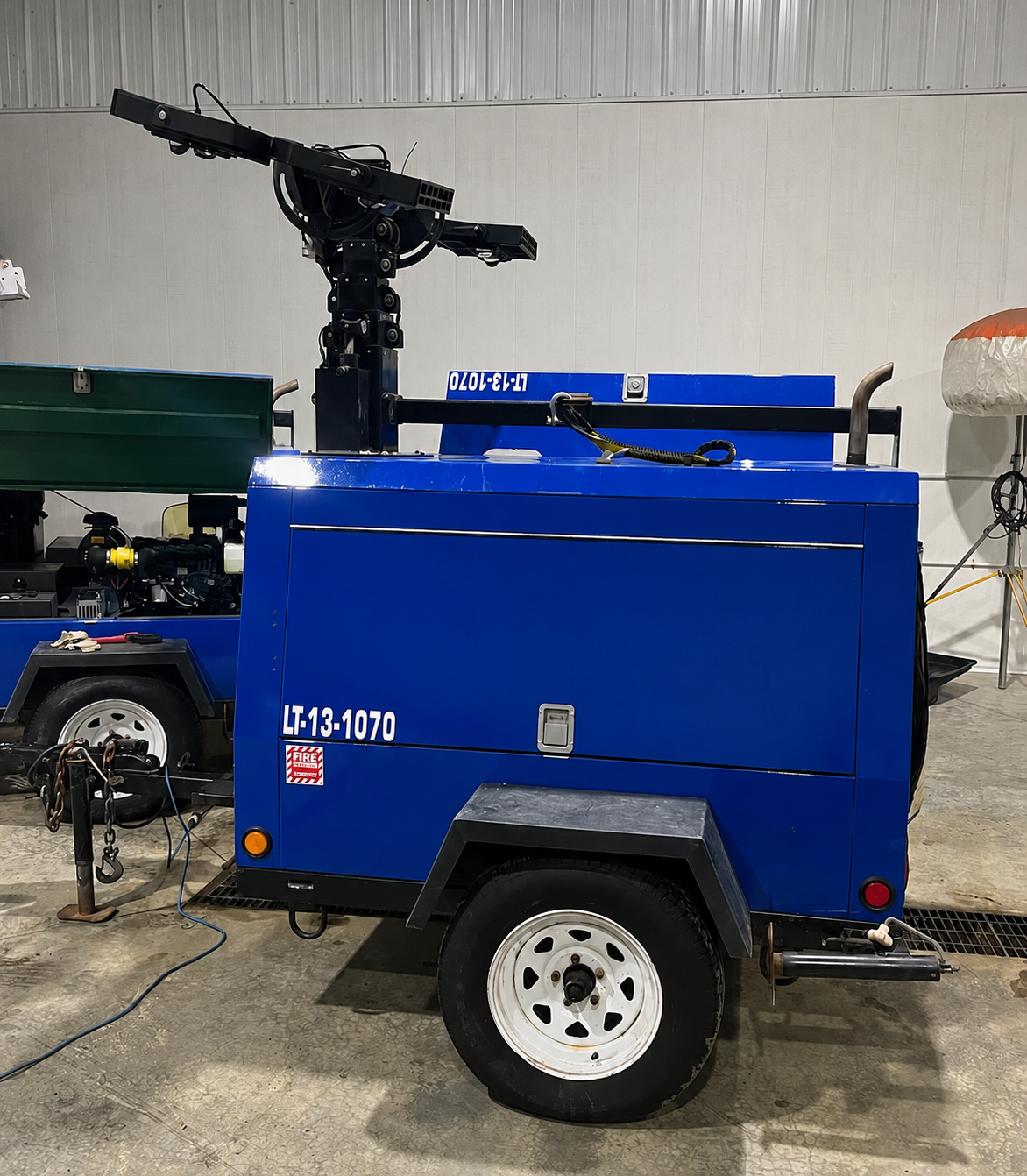 Blue mobile firefighting water pump trailer with a mounted robotic arm in an industrial warehouse.