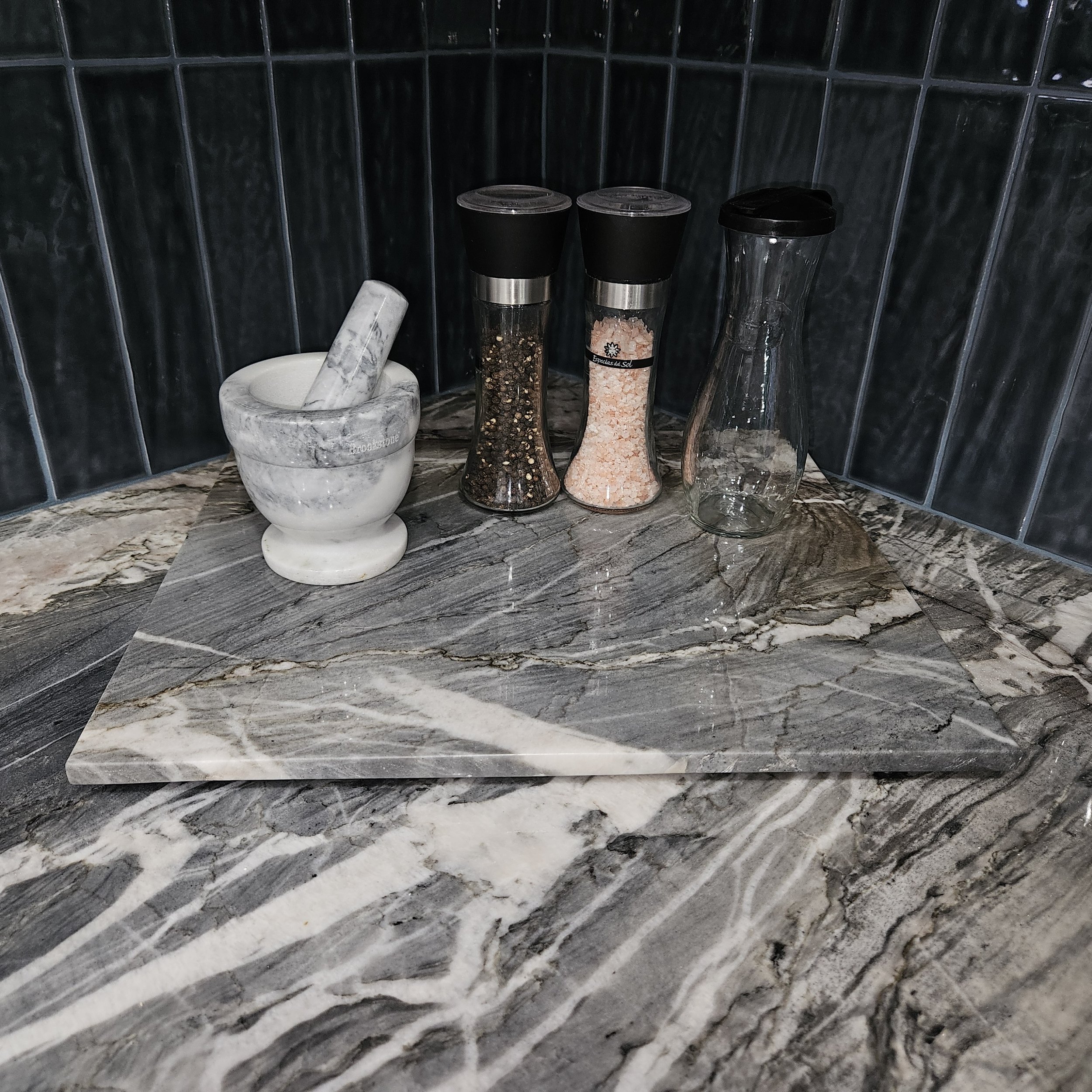 Close-up of a marble countertop with four spice jars and a mortar and pestle against a tiled wall.