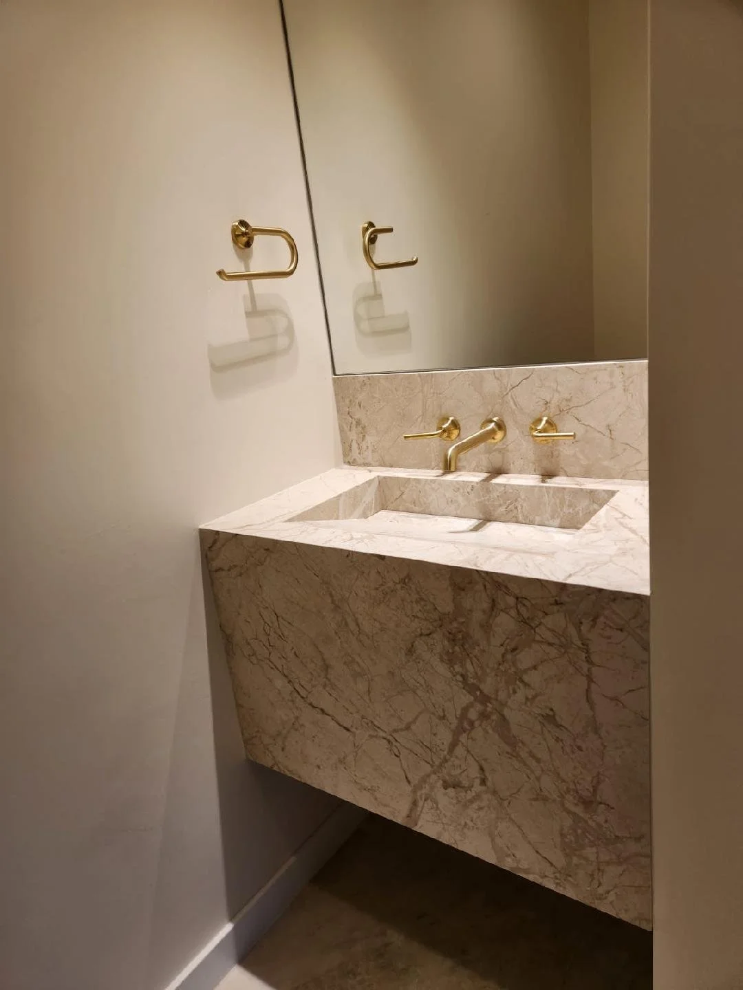Bathroom sink with marble countertop and gold fixtures, mirror, and wall-mounted gold towel hooks.