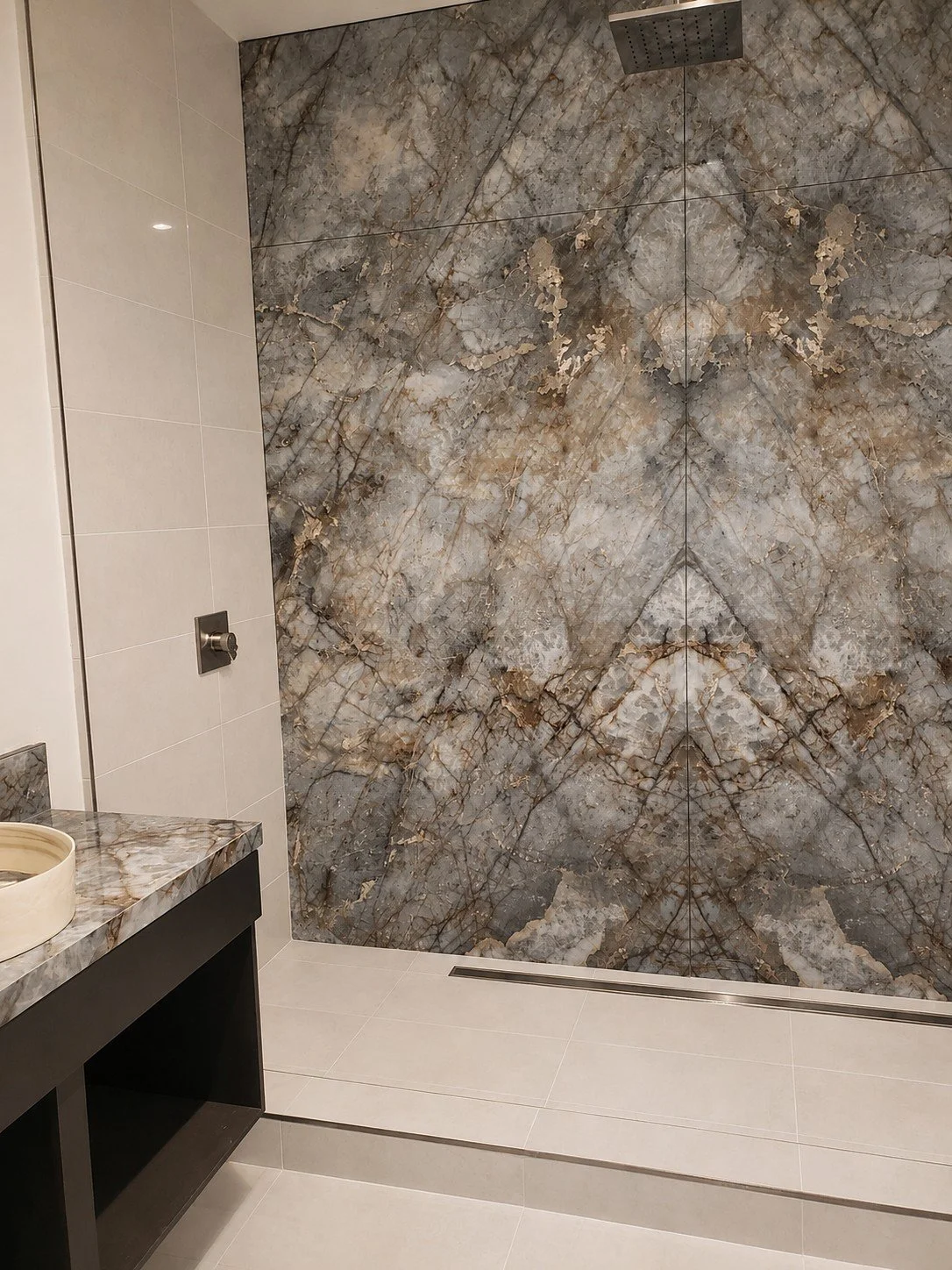 Modern bathroom with a large marble accent wall in shades of gray, beige, and gold, a dark wood vanity with marble countertop, white tiled floor, and a rainfall showerhead.