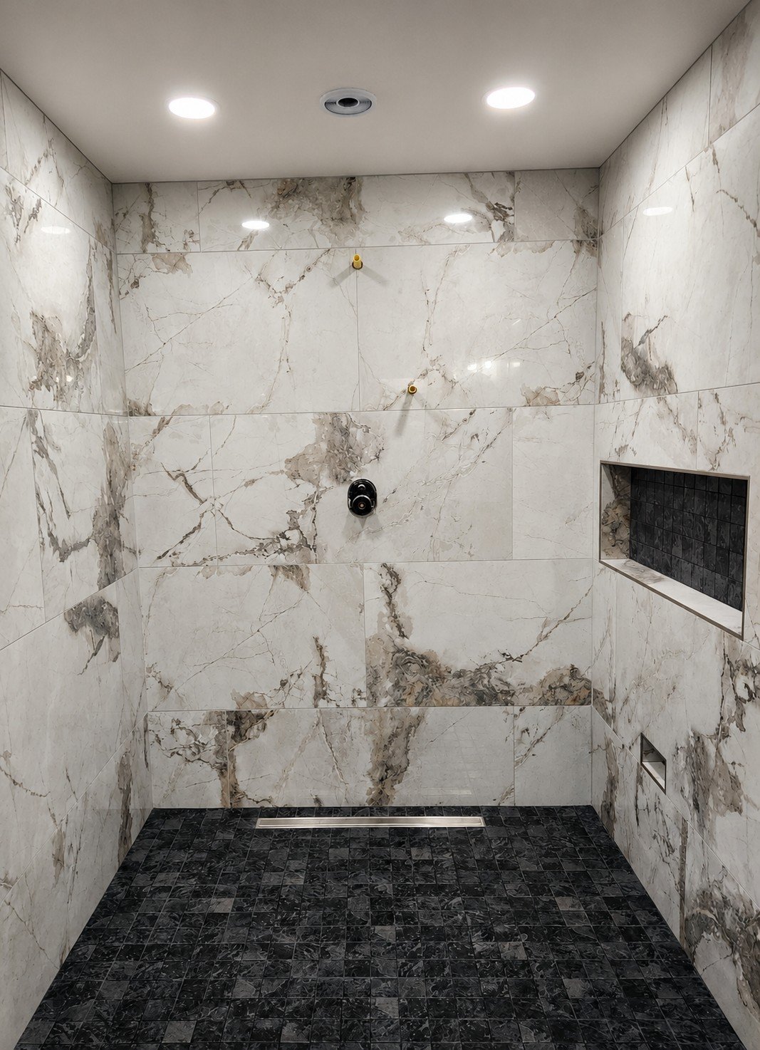 A partially finished walk-in shower with marble walls, a dark tiled floor, a built-in niche with black tiles, and three ceiling lights.