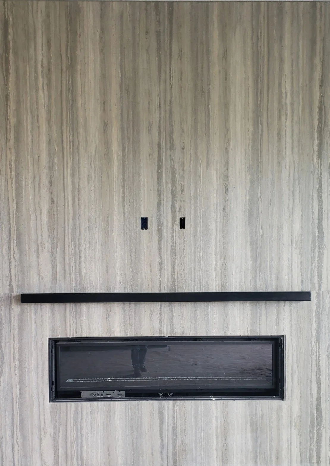 A vertical wooden wall with two electrical outlets and a horizontal black fireplace with a glass cover.