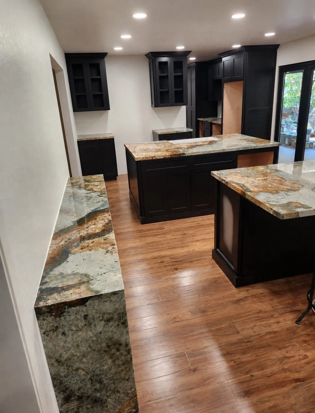 Modern kitchen with black cabinets, granite countertops, and hardwood floors. Open door leads to outdoor patio.