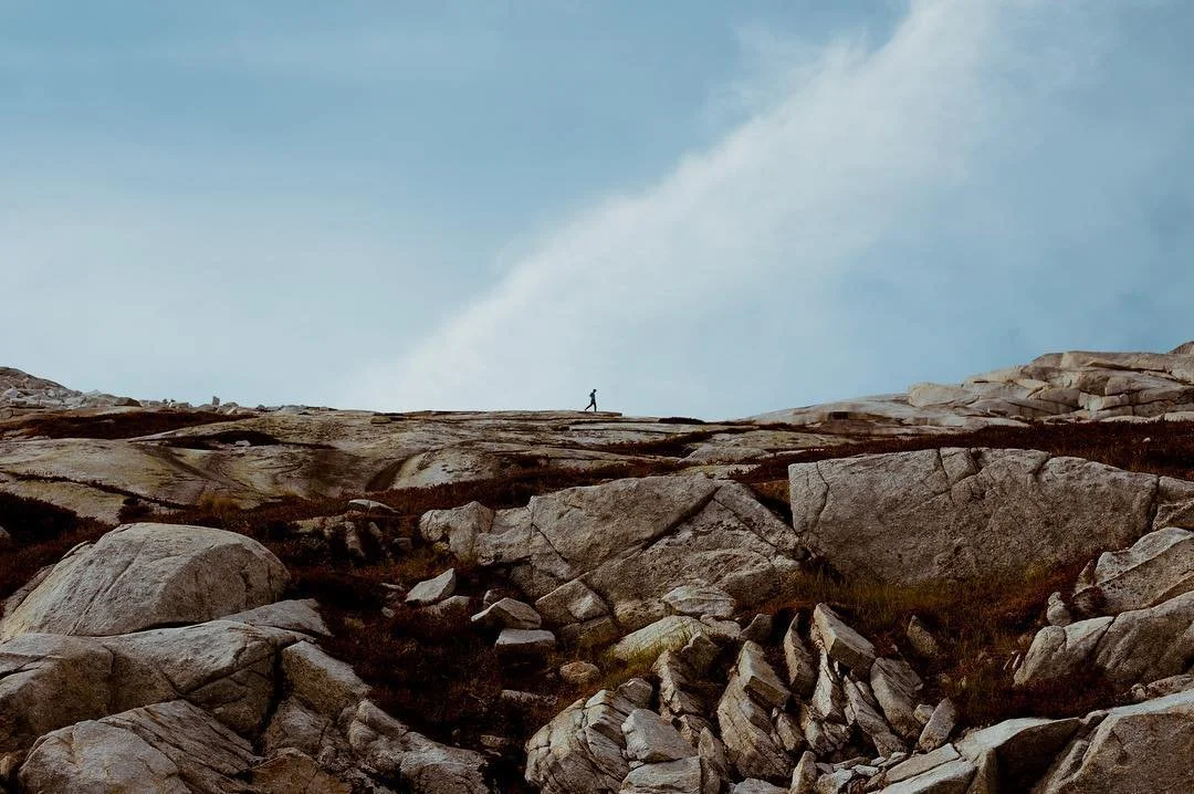 A person hiking on rocky terrain under a cloudy sky.