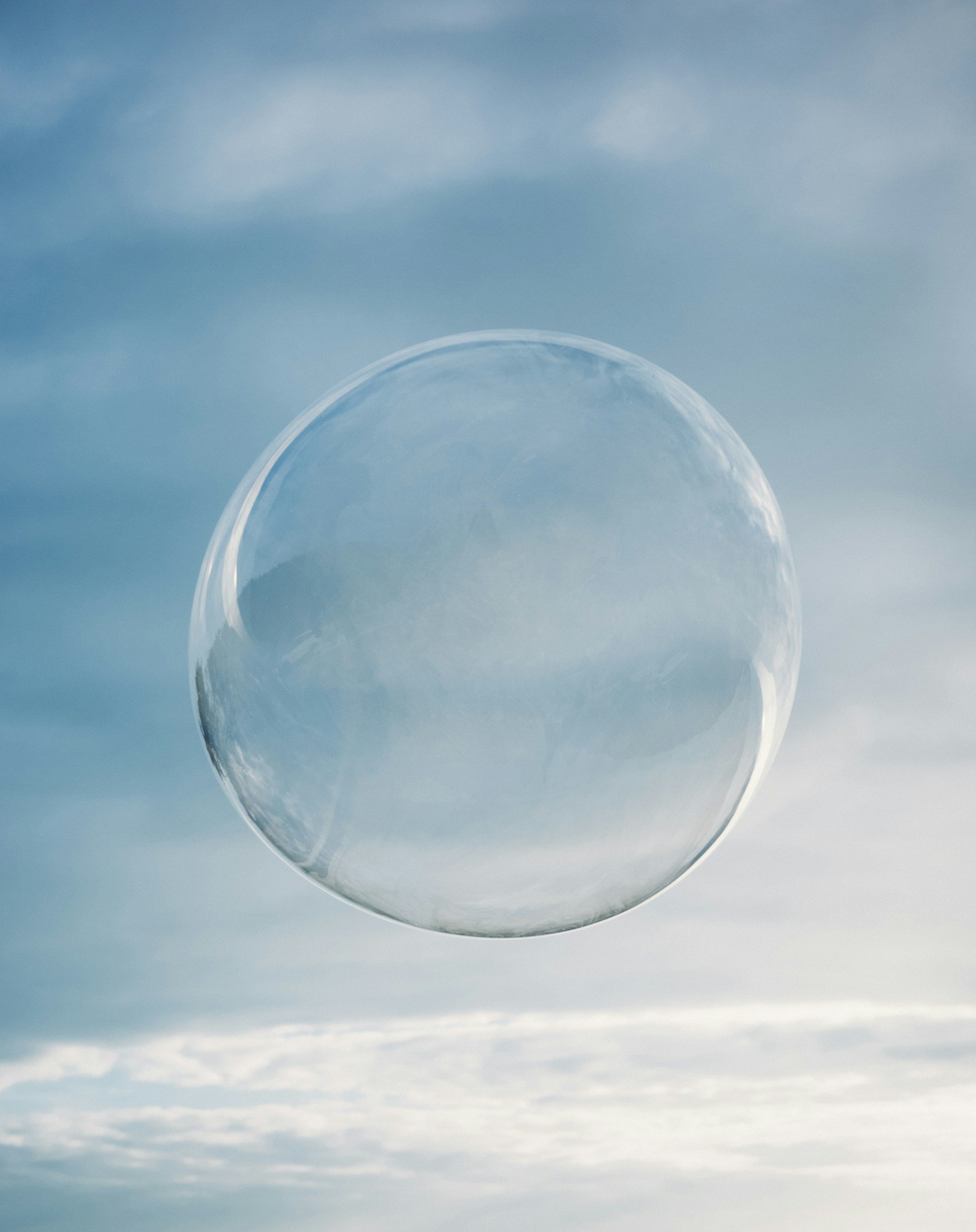 A clear, round glass cup upside-down outside against a backdrop of a cloudy sky and blue clouds.