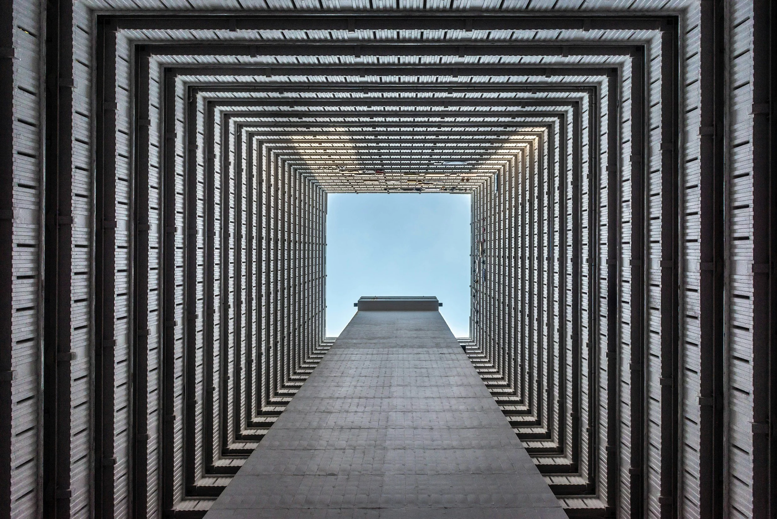 Looking up inside a tall building, seeing multiple rectangular openings lining the walls with a central open sky at the top.
