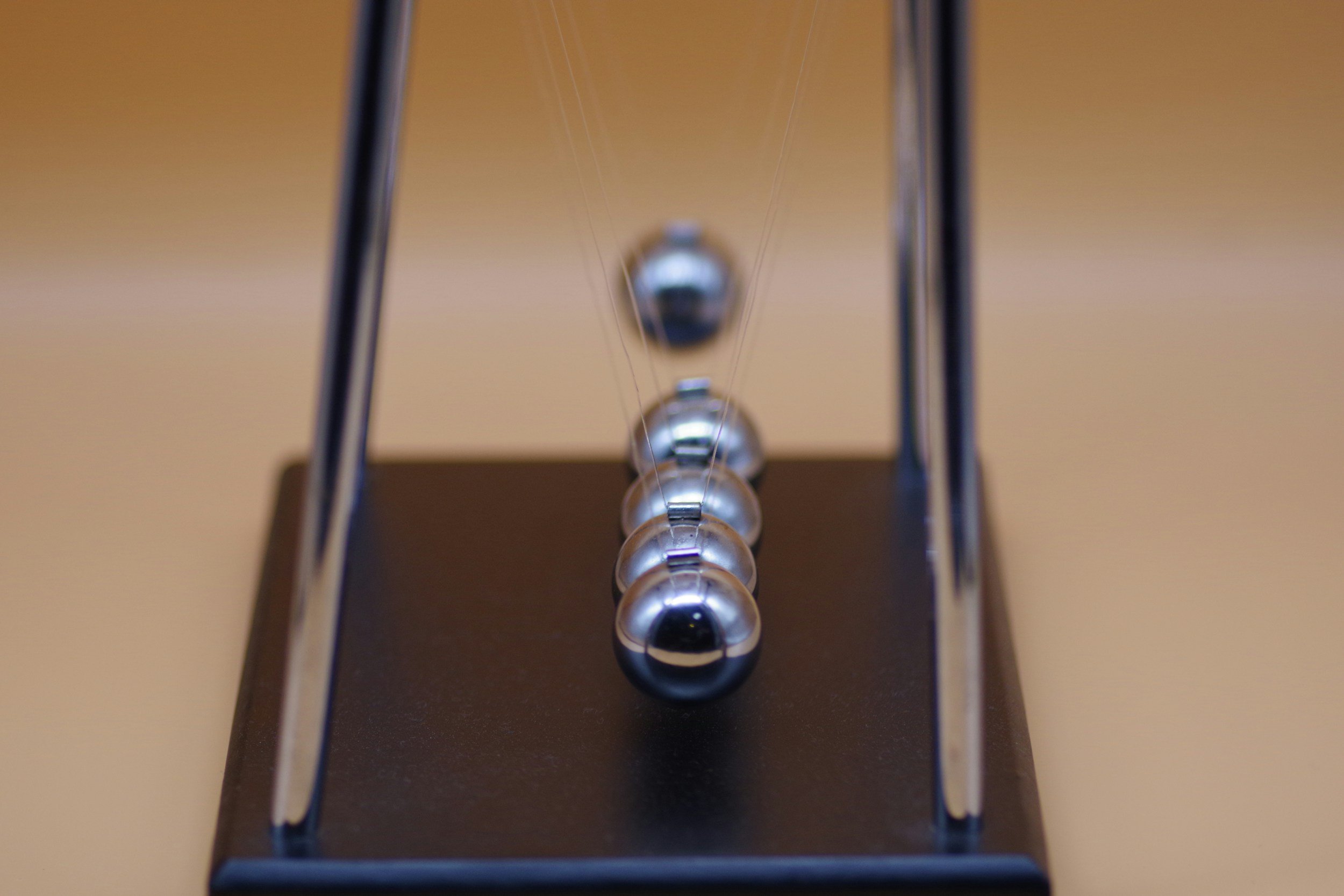 Close-up view of a Newton's cradle with metallic spheres suspended by thin wires within a metal or plastic frame.