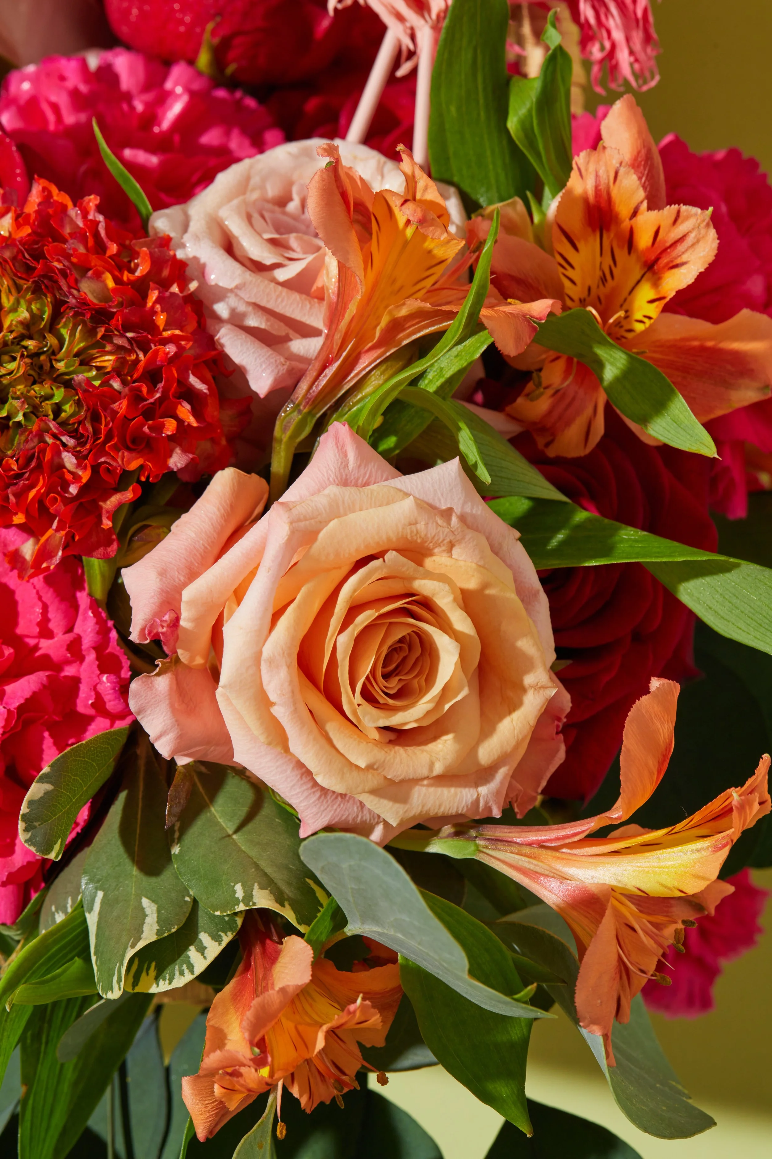Close-up of a bouquet of various flowers, including a peach-colored rose, orange lilies, red hydrangea, pink peony, and green leaves.