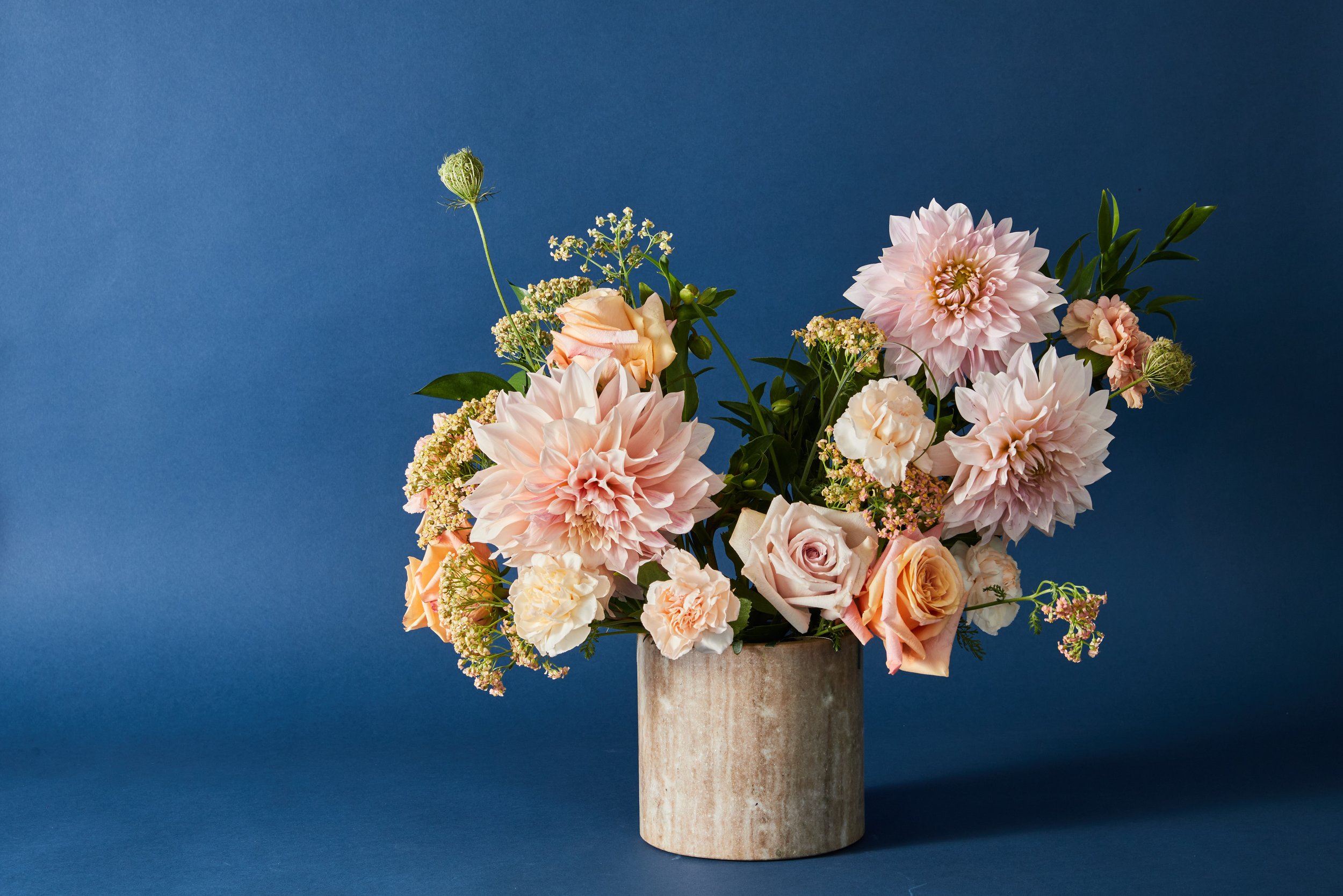 A bouquet of pink and peach flowers in a gray vase against a blue background.
