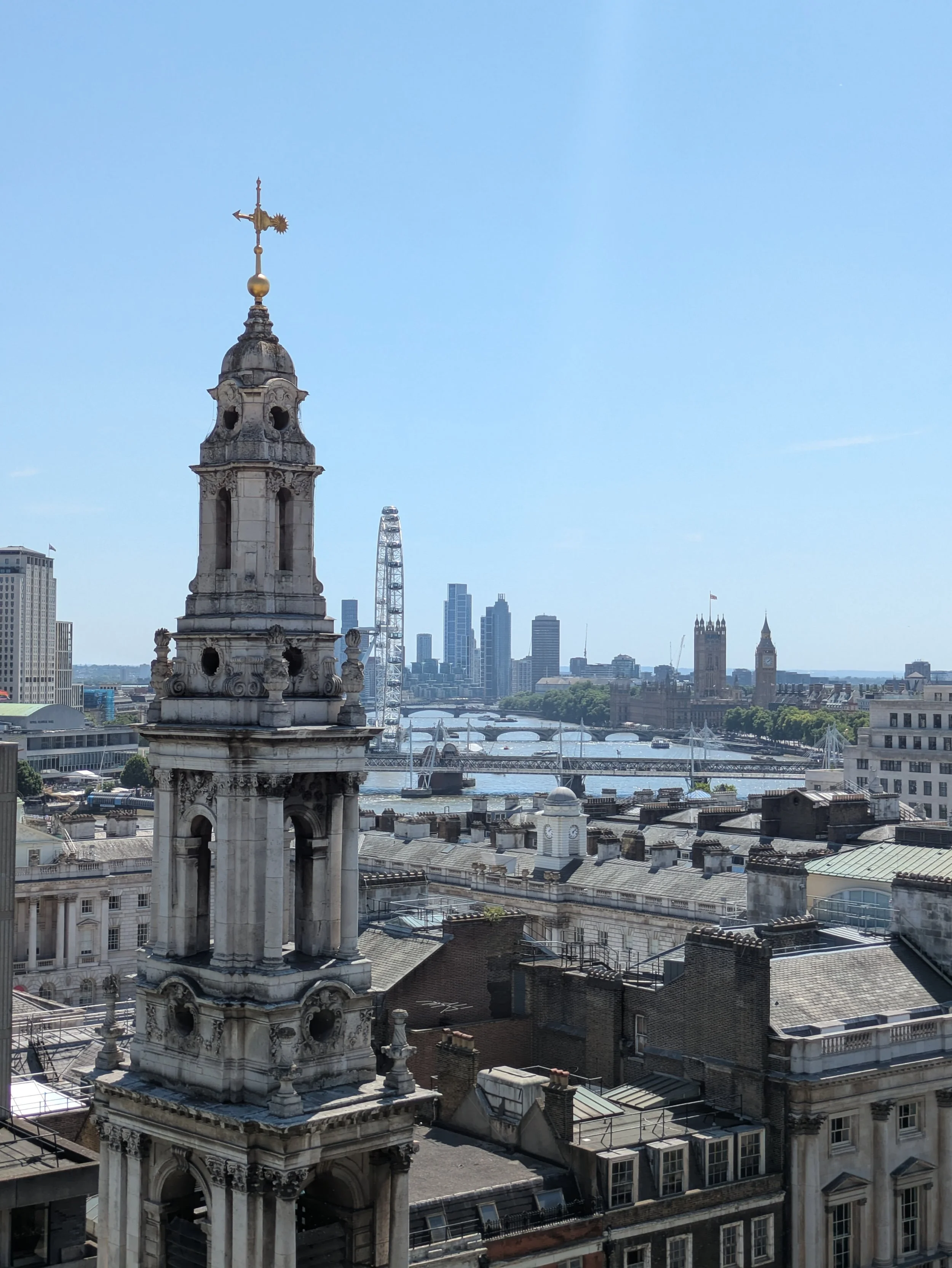 View of London skyline with historic building and tower in the foreground, the London Eye in the background, and Big Ben clock tower visible.