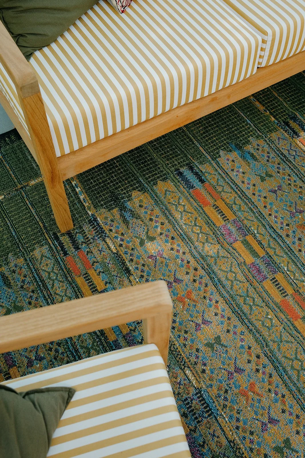 A view of chairs with wooden frames and striped yellow and white cushions over a patterned colorful rug.