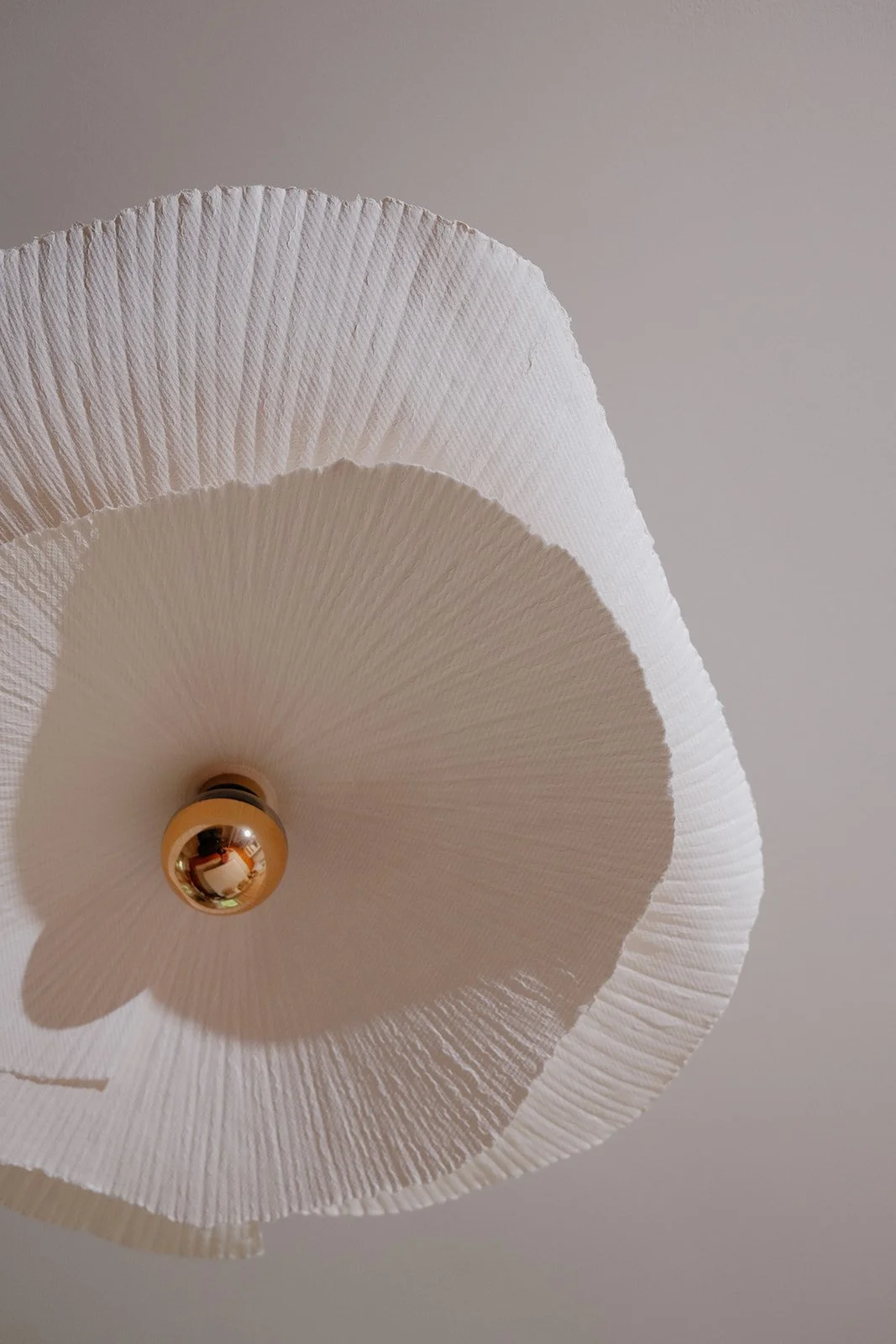Close-up of a white paper lantern ceiling light fixture with a shiny gold bulb socket against a plain ceiling.