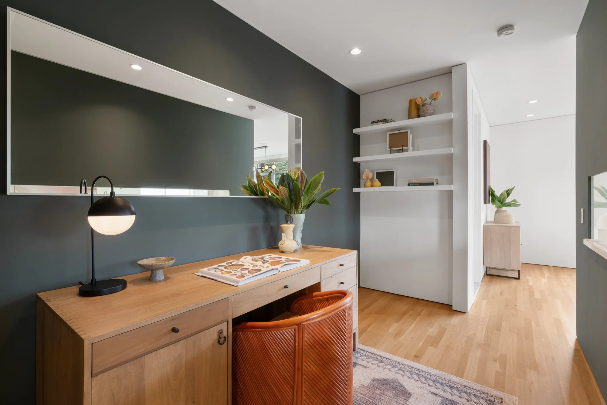 Modern living room with wooden sideboard, decorative plants, shelves with books and decor, and a mirror on the wall.