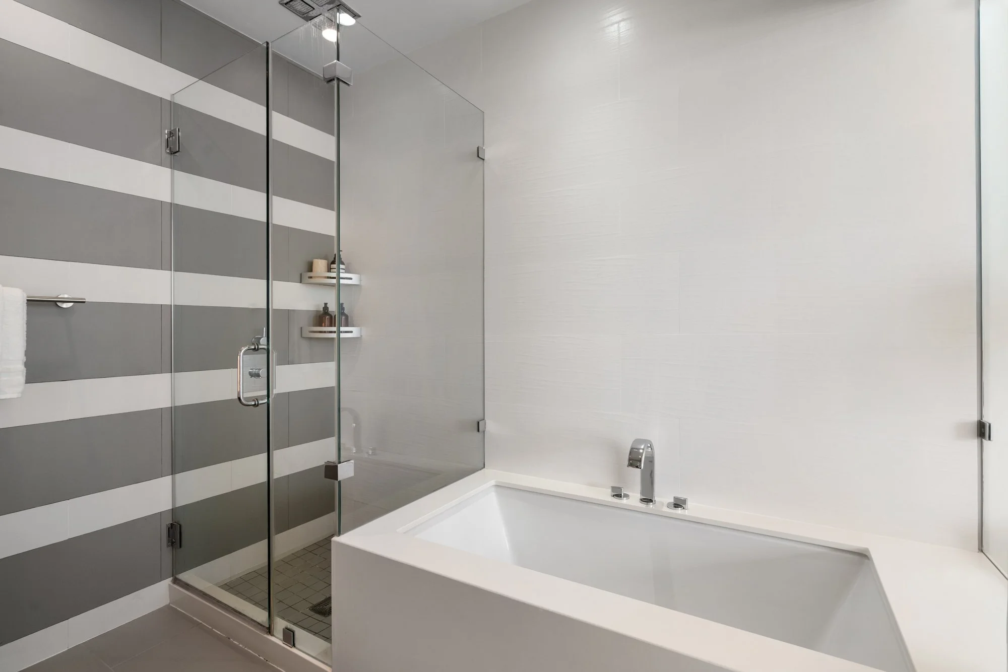 Modern bathroom with a glass-enclosed shower, striped gray and white walls, and a built-in bathtub with a chrome faucet.