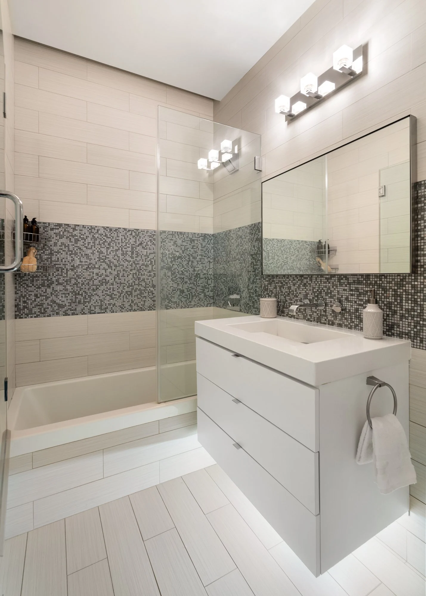 Modern bathroom with a walk-in shower, large mirror, white vanity with a sink, and neutral colored tiles with a mosaic accent wall.