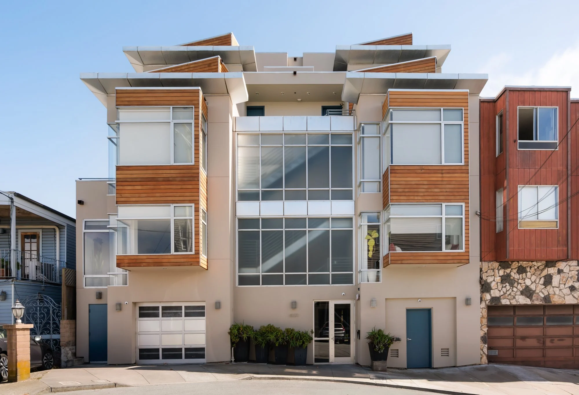 Front view of a modern multi-story apartment building with large glass windows, wood paneling, and a garage on the ground floor, with neighboring buildings visible on each side.