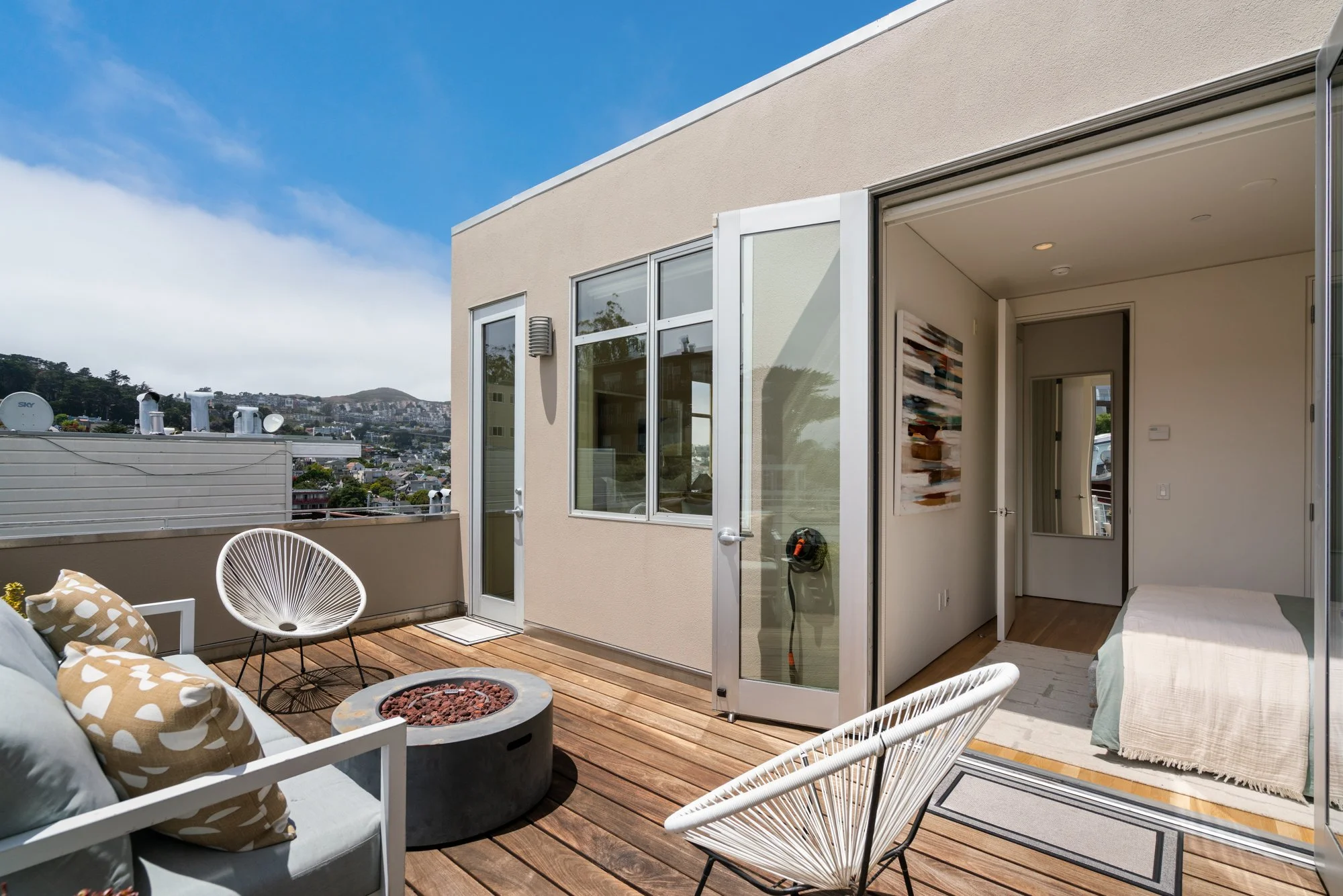 Outdoor balcony with seating area, fire pit, and view of cityscape and hills.