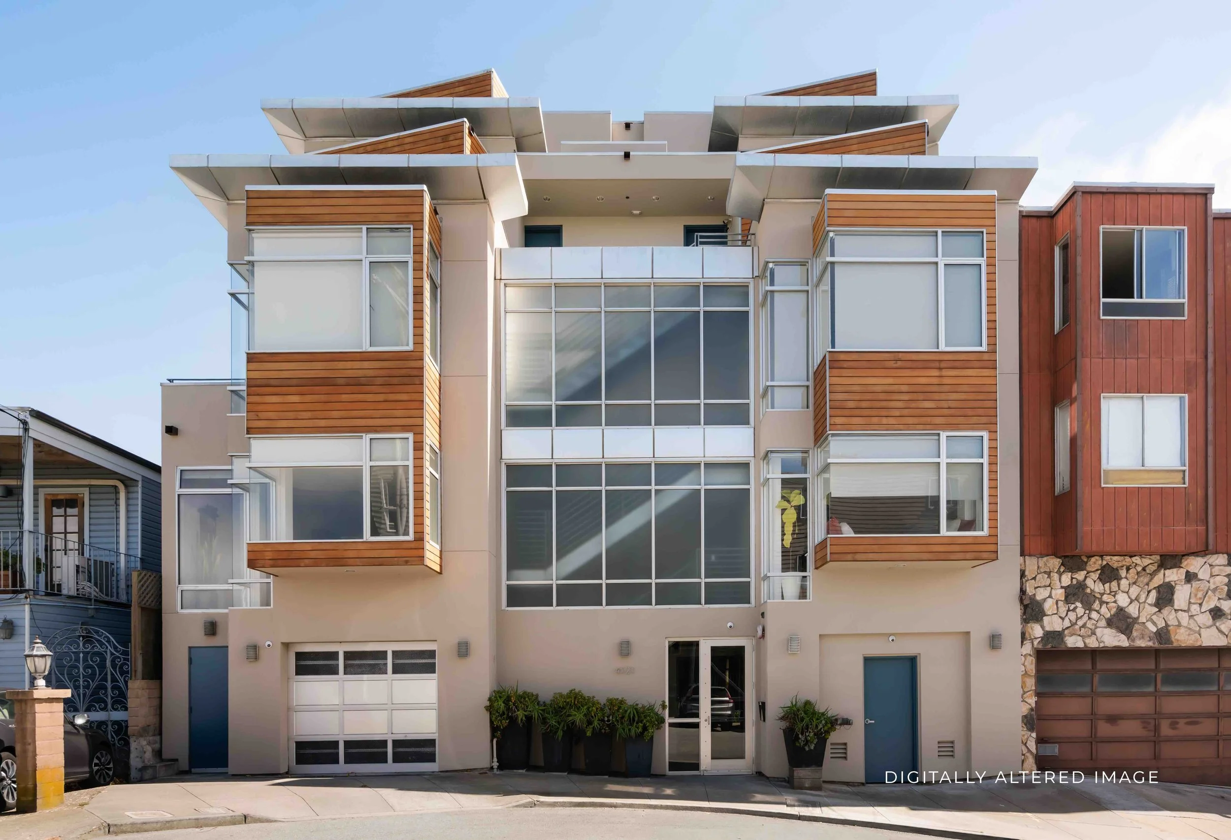 A modern multi-story residential building featuring large glass windows and wooden accents, with a stone foundation and small potted plants at the entrance, under a clear blue sky.