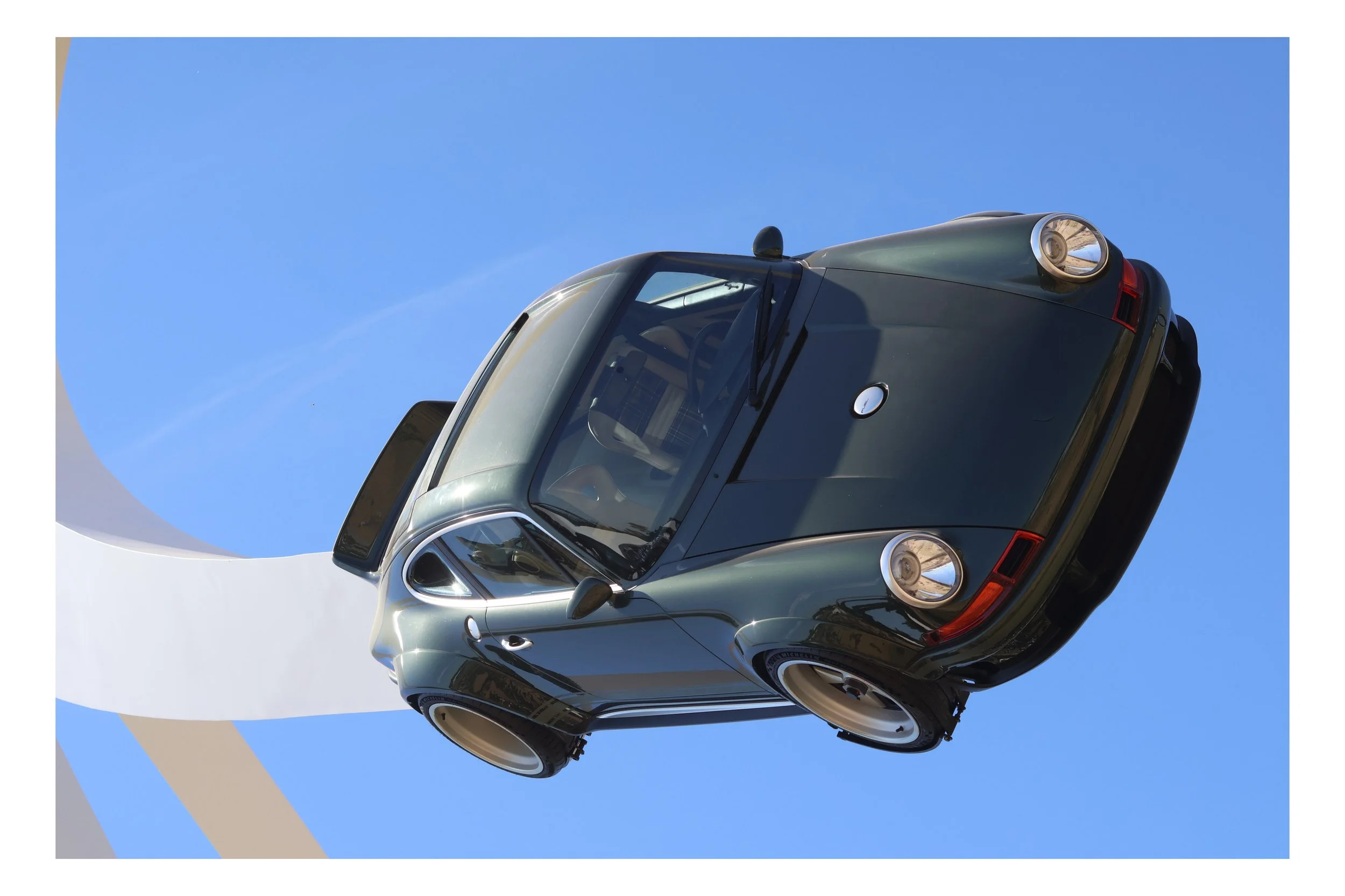 A Tesla Model S in metallic green color parked under a clear blue sky with white clouds.