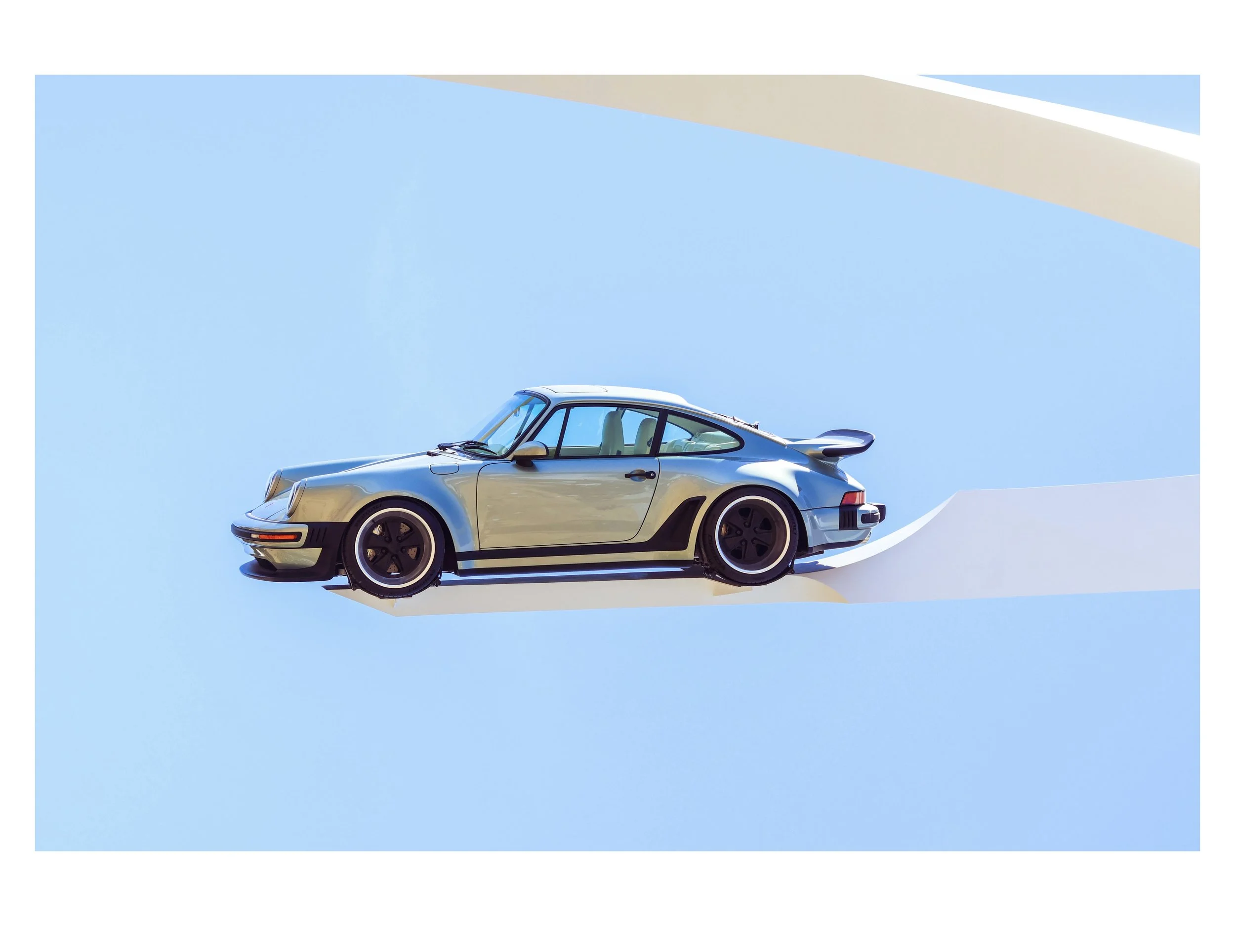 A vintage blue sports car on a white platform against a light blue background.