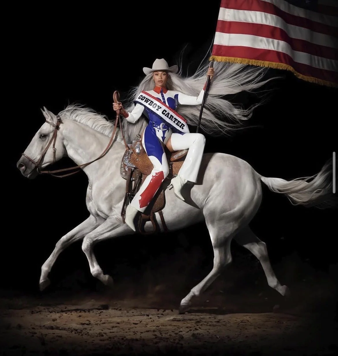 A woman dressed in a cowgirl outfit, riding a white horse in a dramatic scene holding an American flag, with a black background.