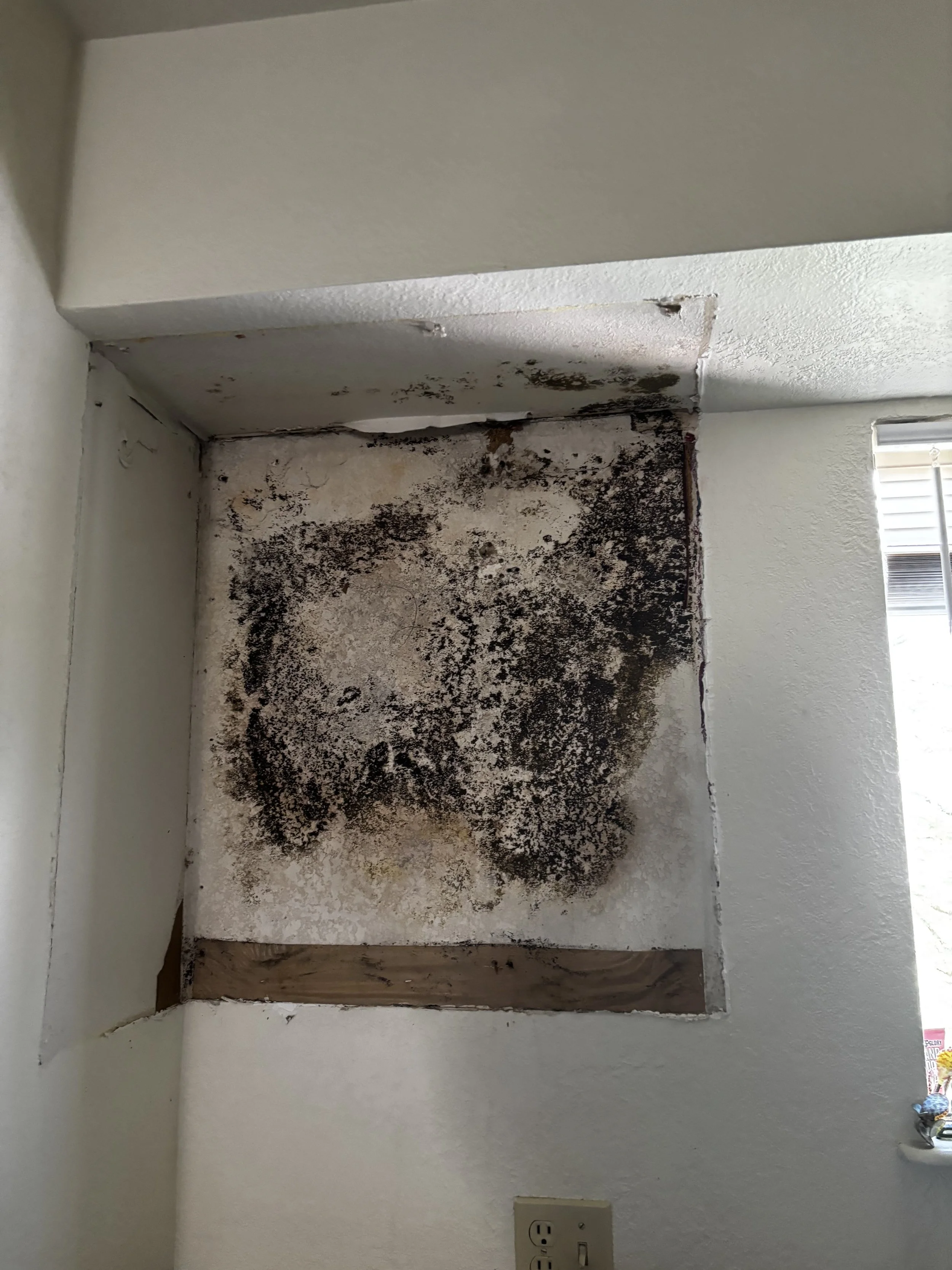Room damage with black mold and soot on the wall beneath a removed cabinet, with an electrical outlet visible at the bottom.