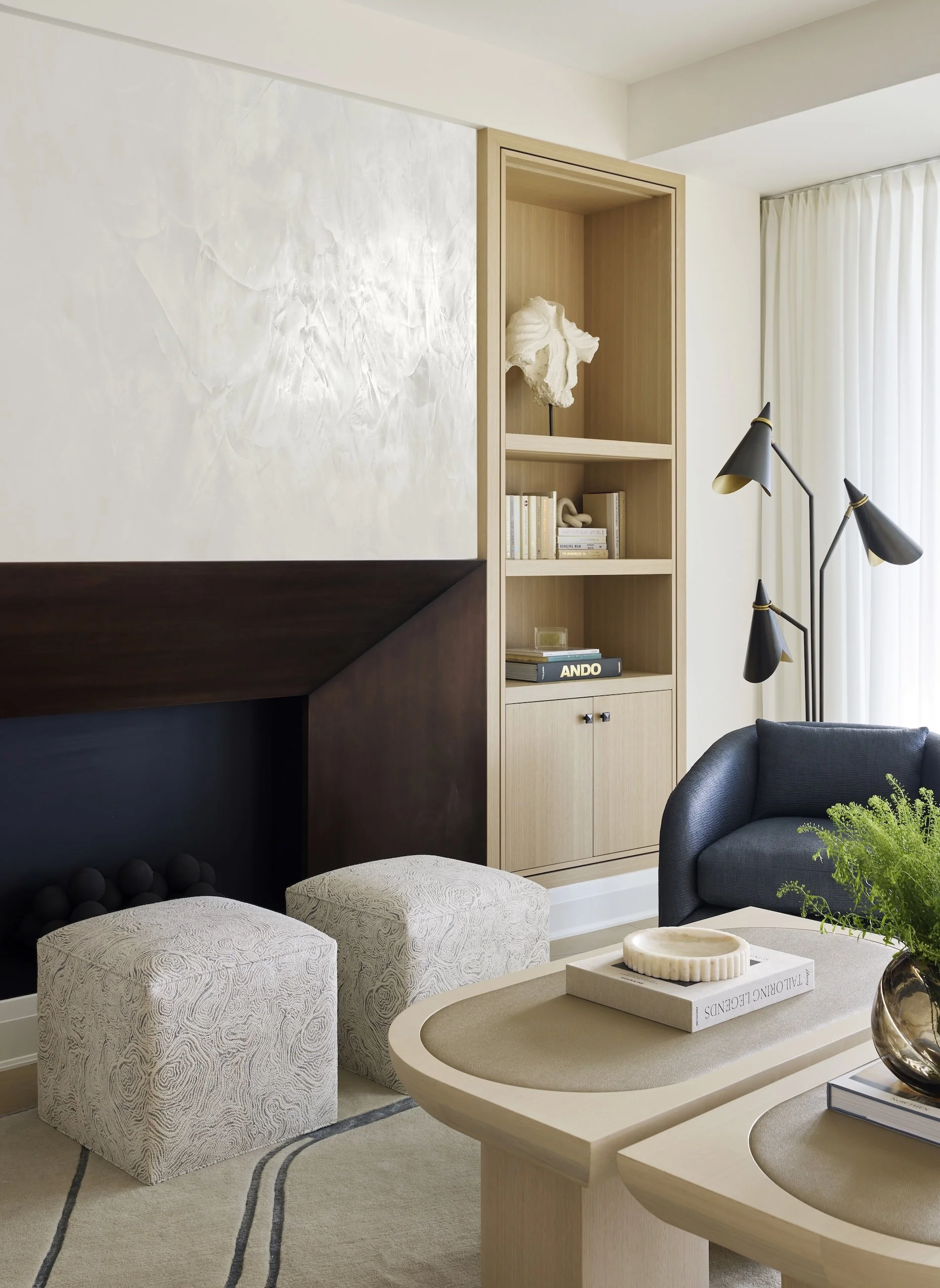 Modern living room with beige and black furniture, a built-in bookshelf with art and books, black floor lamps, and a beige rug with black stripes.