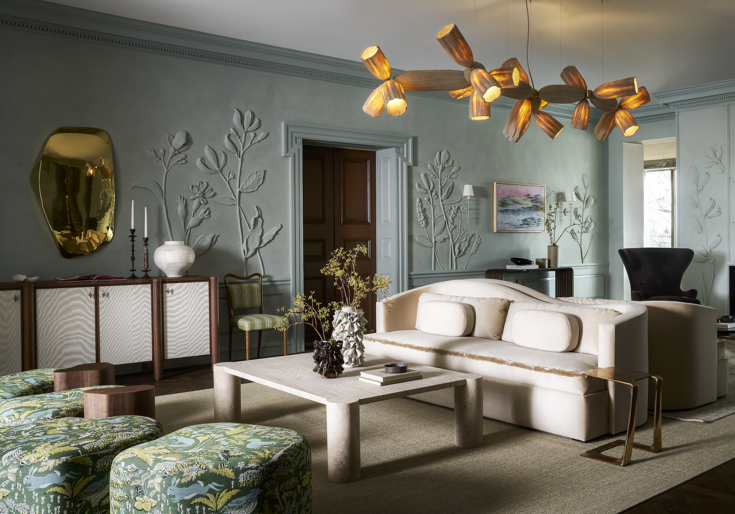Living room with modern decor, including a white sofa, glass and wood table, green patterned ottomans, wall art, and a striking wooden chandelier.