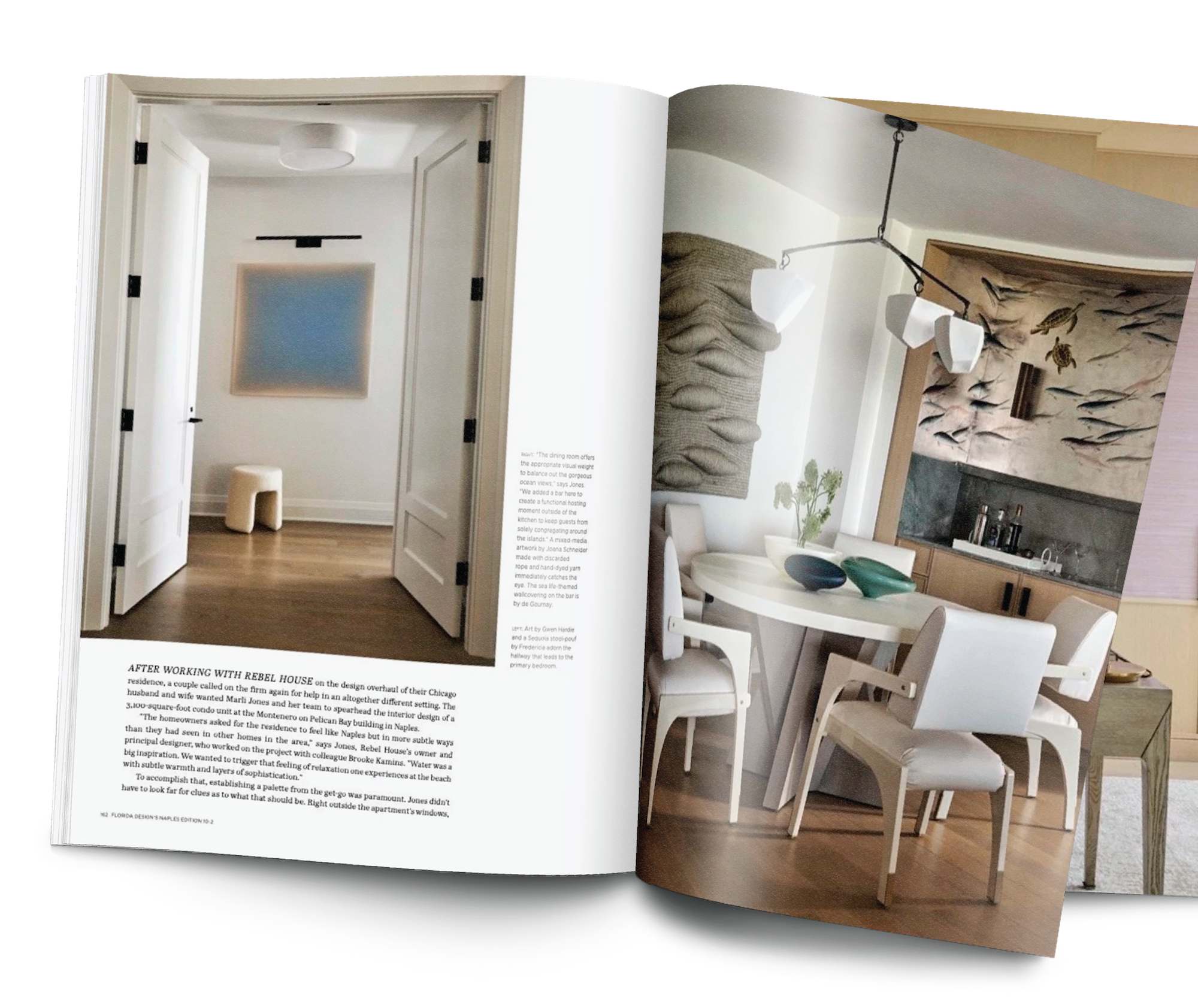 Open magazine showing a dining room with a wooden floor, a white table with four white chairs, and a mural of fish on the wall. The magazine is on a wooden surface.