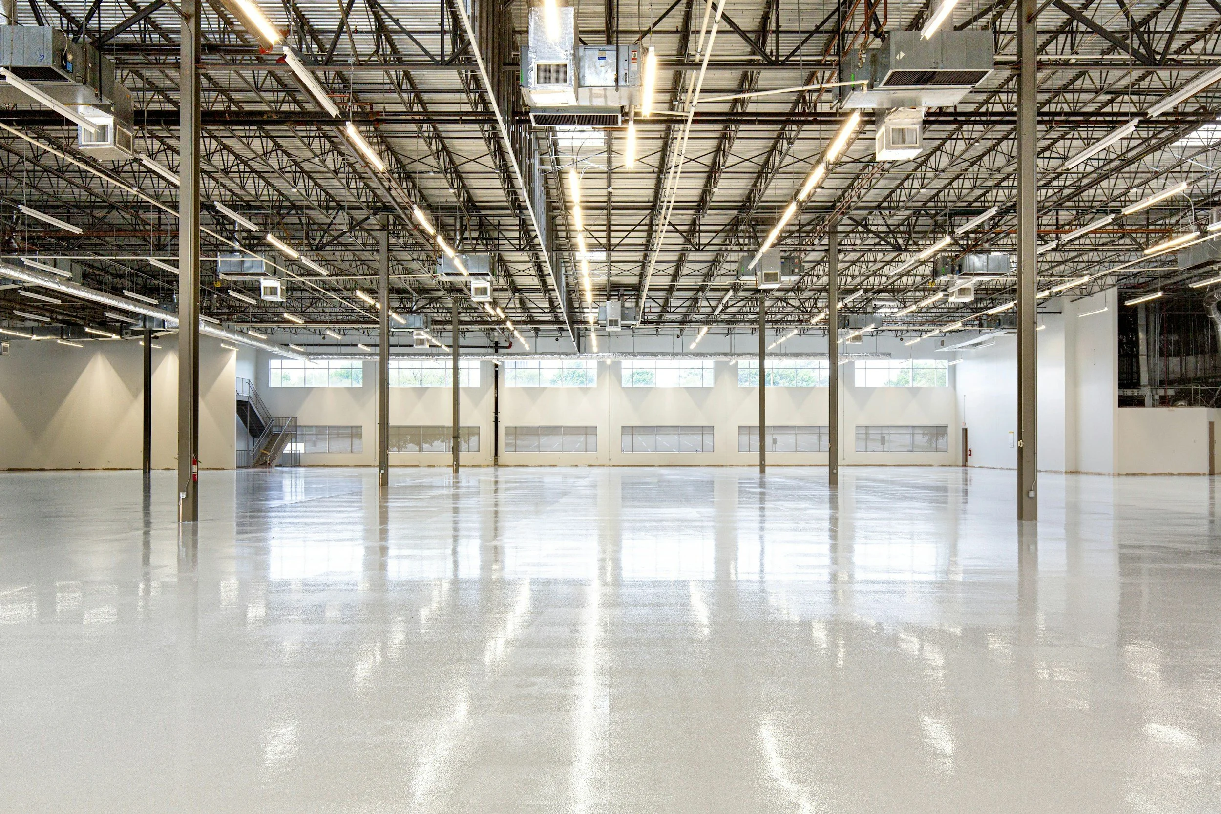 Empty industrial warehouse with high ceilings, exposed metal beams, and bright lighting.