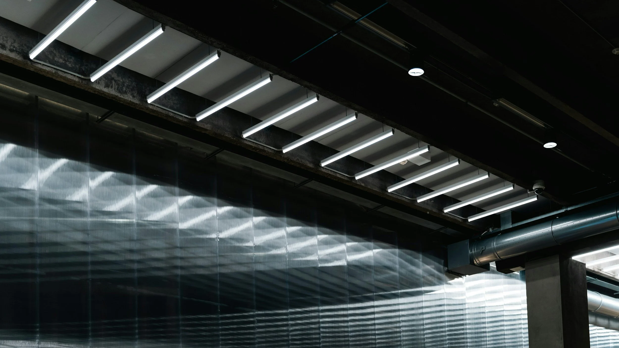 Modern ceiling with linear white LED light fixtures and metallic wall panels with a reflective surface.