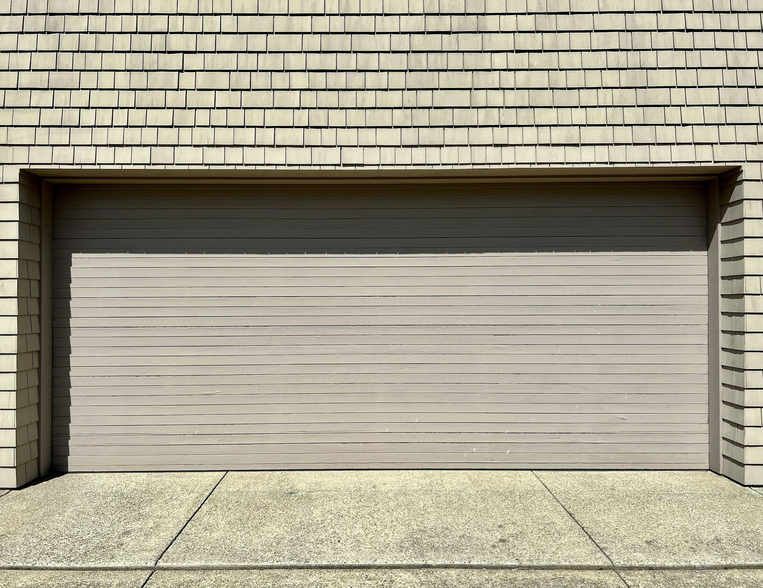A closed beige garage door surrounded by cream-colored brick walls, with a concrete sidewalk in front.