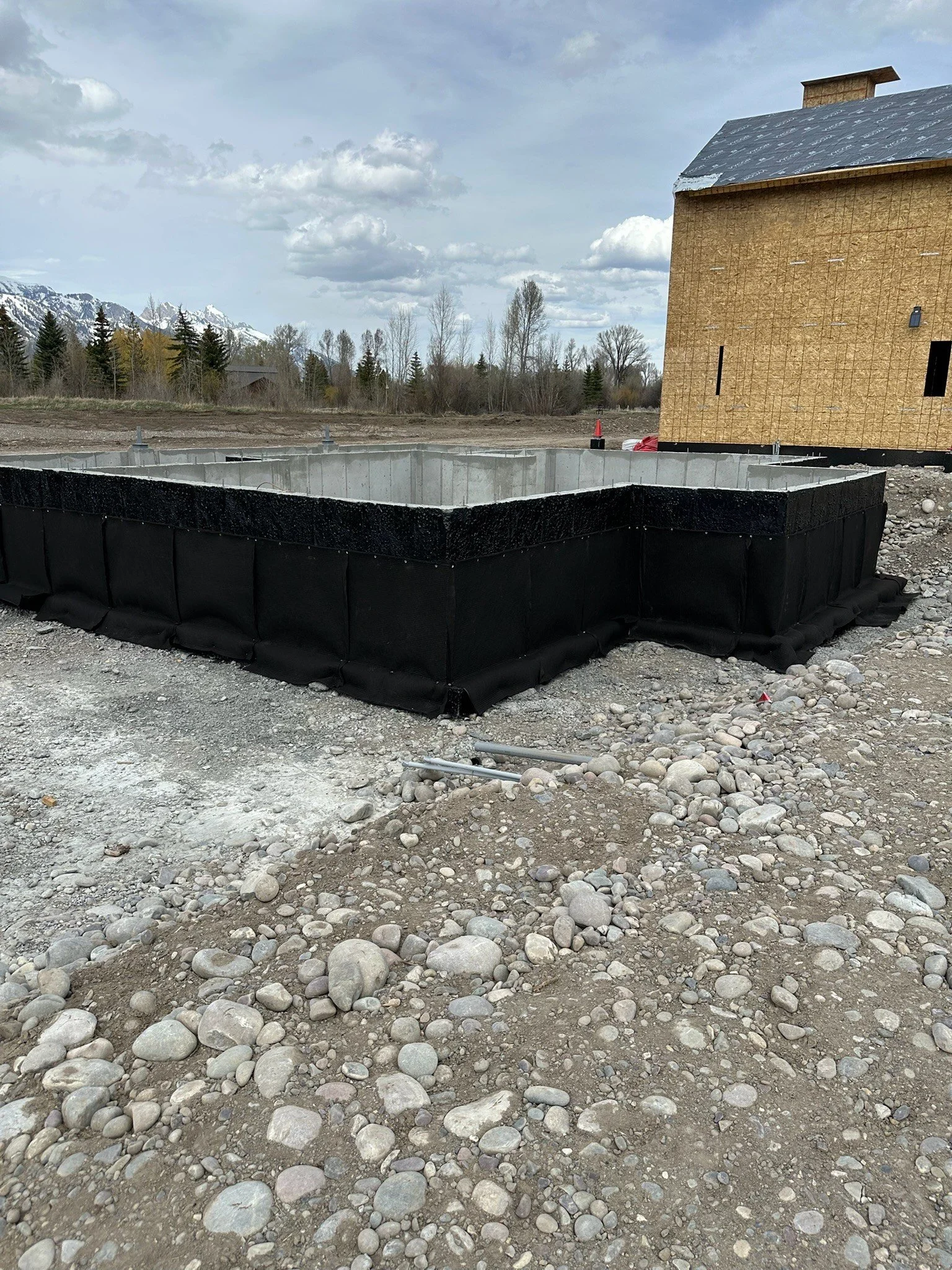 Construction site with a building under construction, foundation excavation, and a gravel ground with rocks.